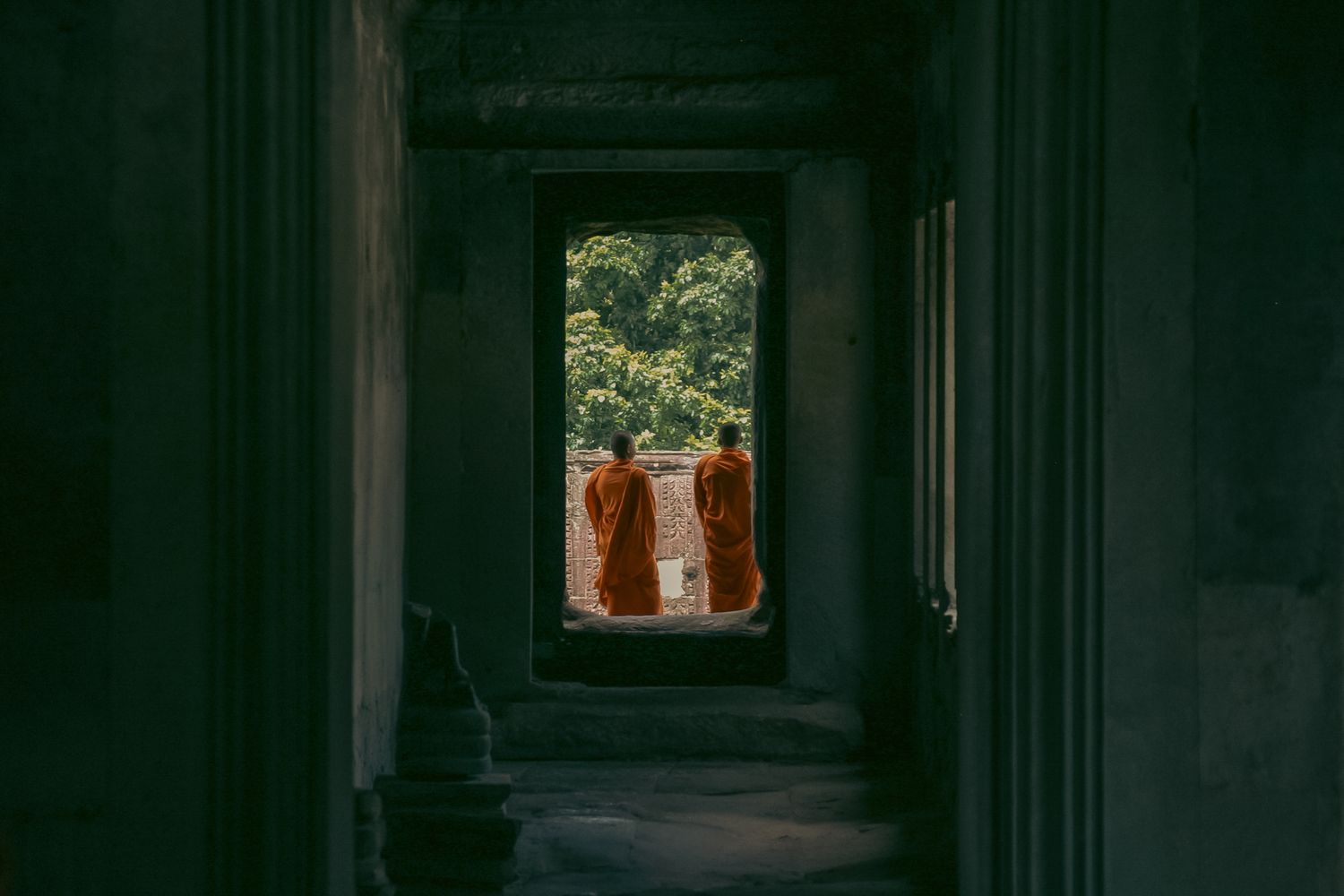 Dark corridor in Angkor Wat with arched windows and columns creating dramatic shadows and light.