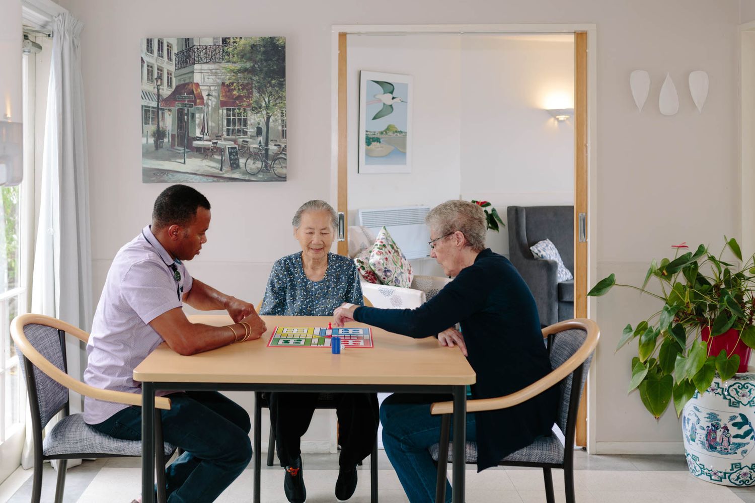 Rest home residents and staff interacting in a bright, modern common area with artwork on walls.