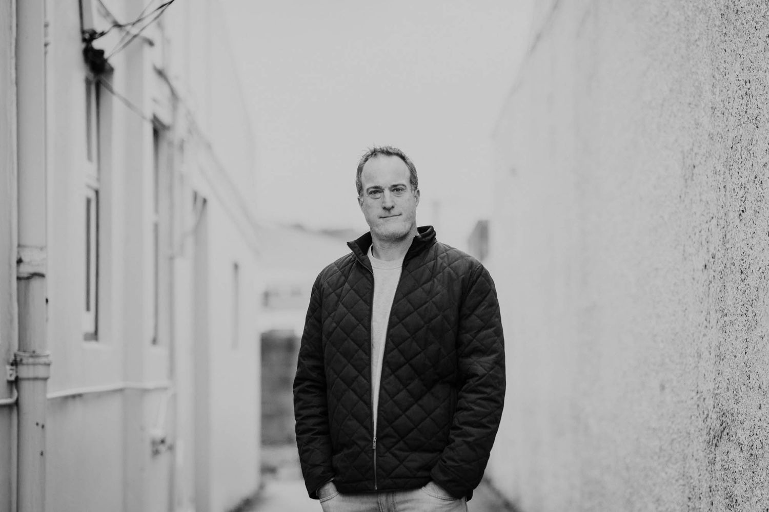 Black and white portrait of Tim Lee from Latitude Lighting standing against textured wall wearing quilted jacket.