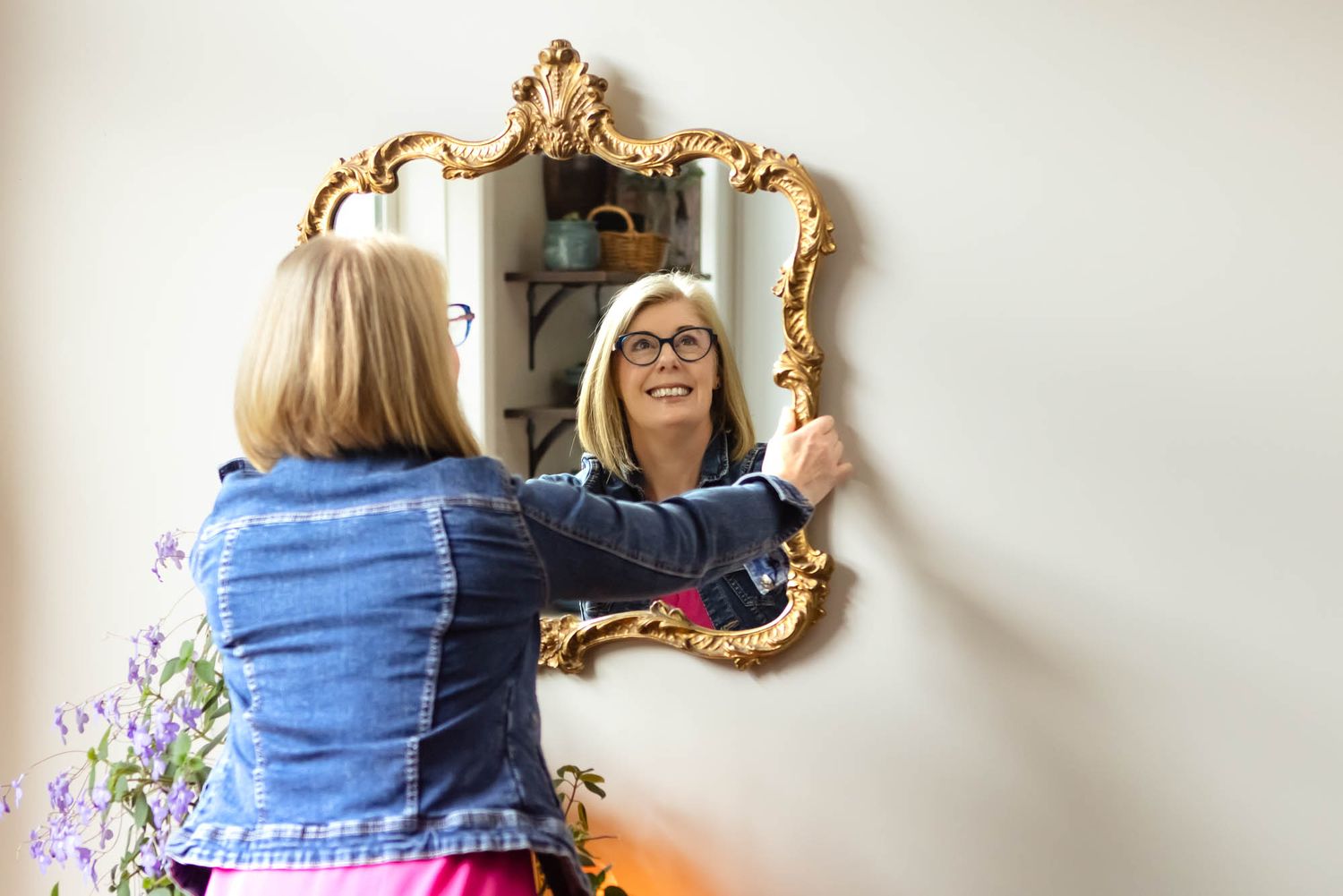 Decorative gold mirror mounted on white wall with person arranging items nearby.