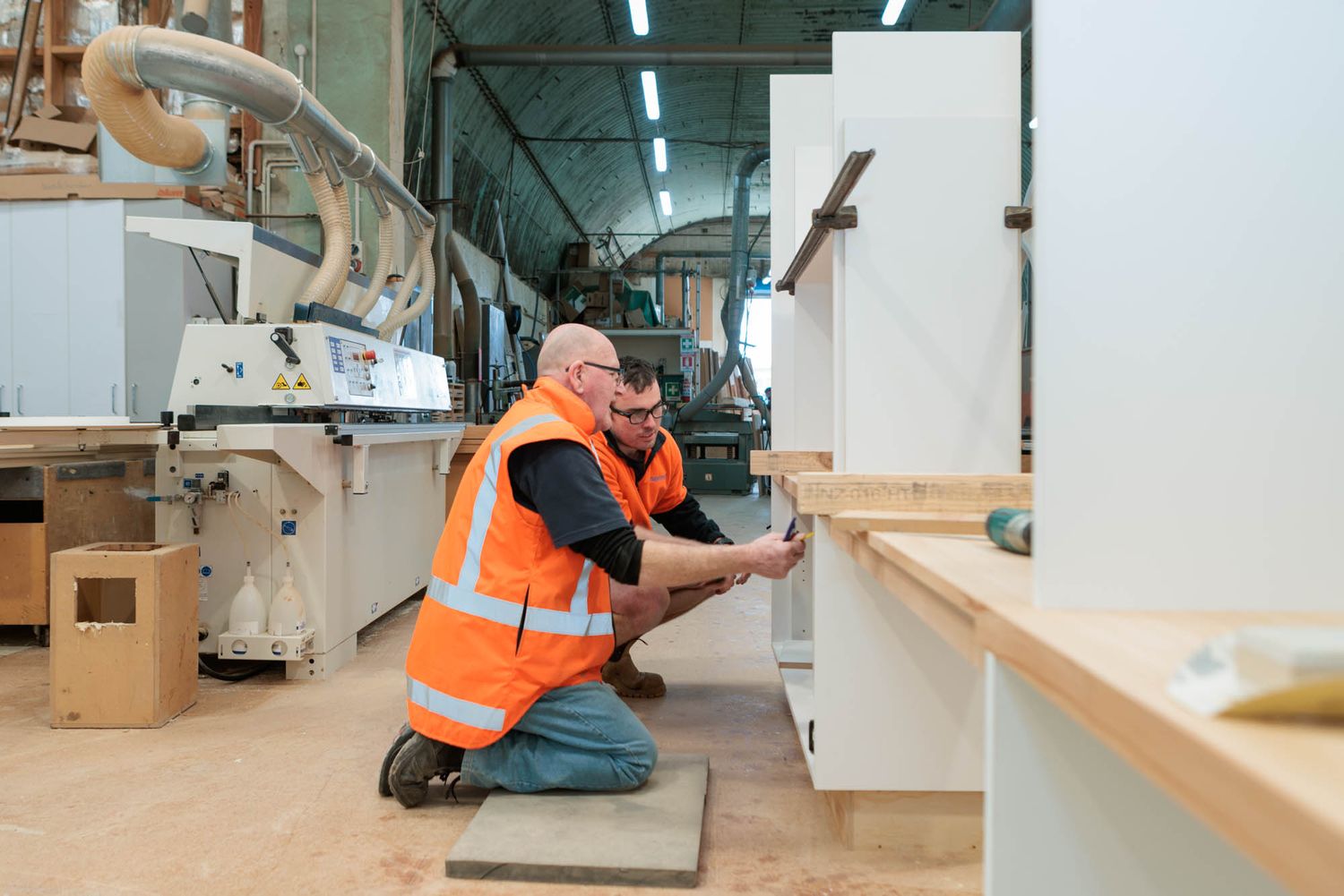Maycroft workers in safety vests installing wooden shelving units in commercial space.