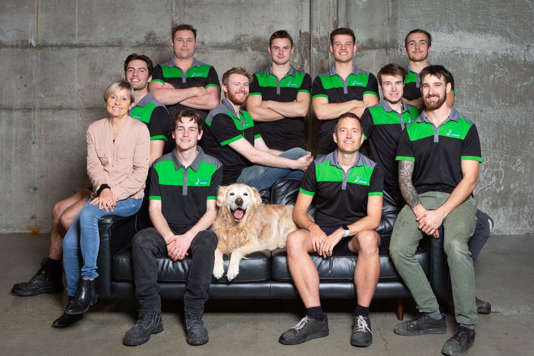 Team photo of staff members wearing green and black uniforms sitting on a gray couch.