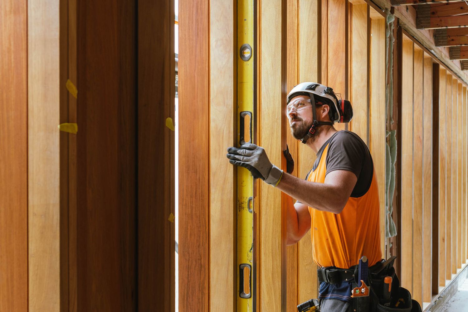 Maycroft worker in safety gear inspect wooden framing in a construction site hallway.