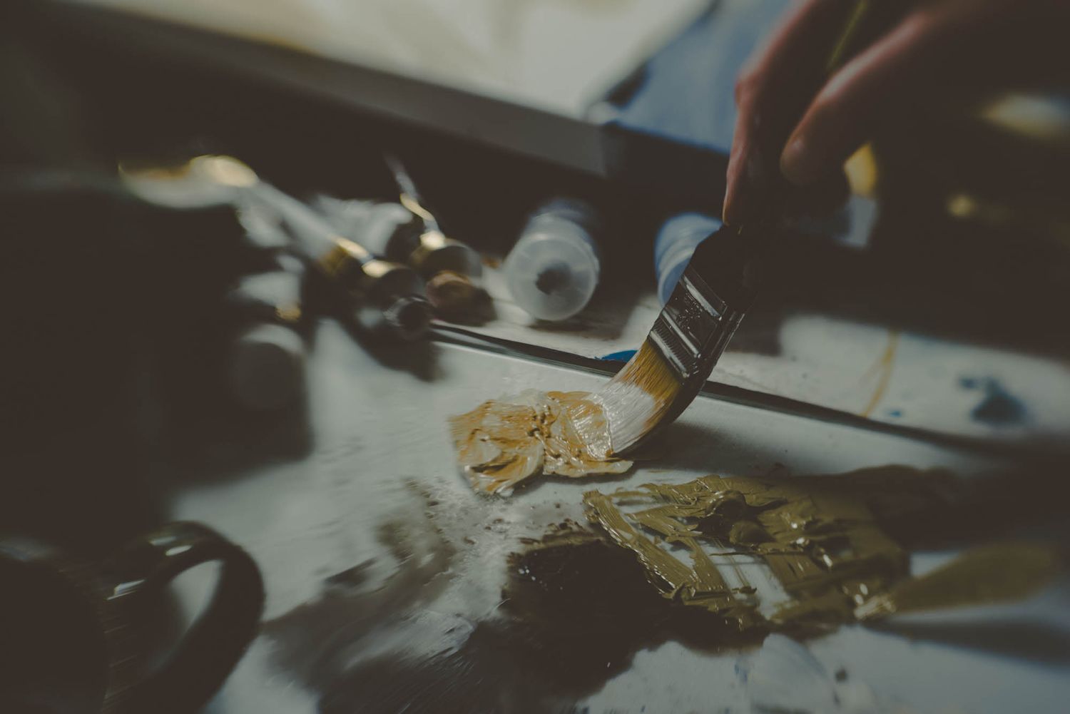 Close-up shot of a paintbrush applying gold paint to an artistic surface.
