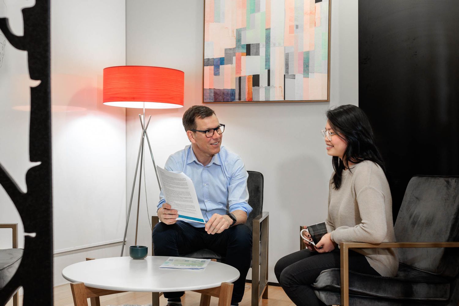 Two professionals having a discussion in a modern office setting with red lamp.