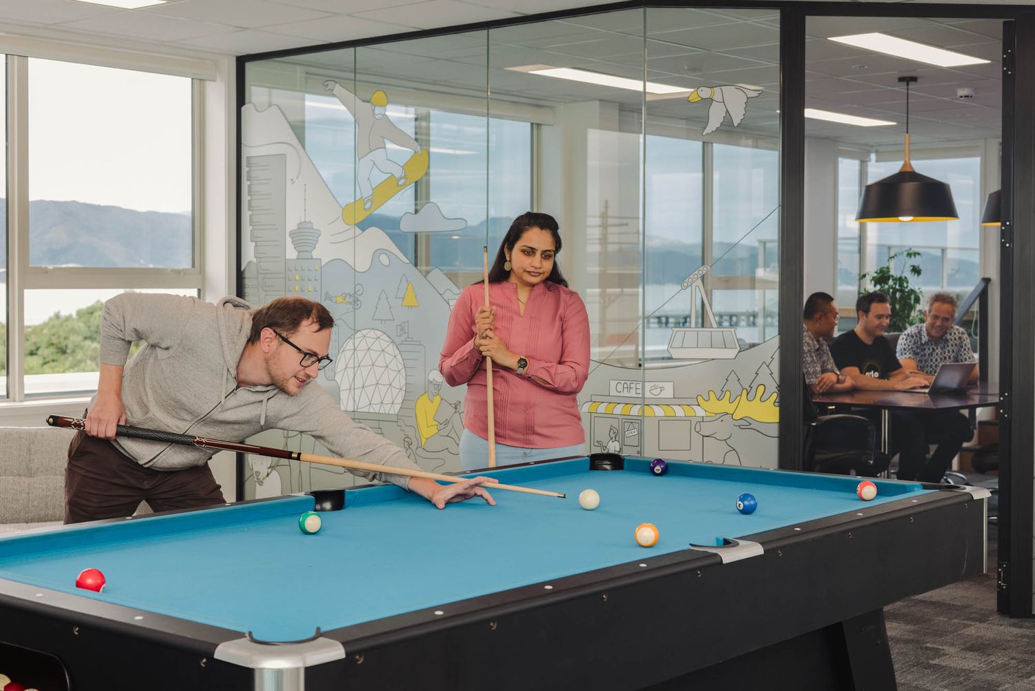 Modern office recreation space at Arlo with pool table and large windows overlooking mountains.