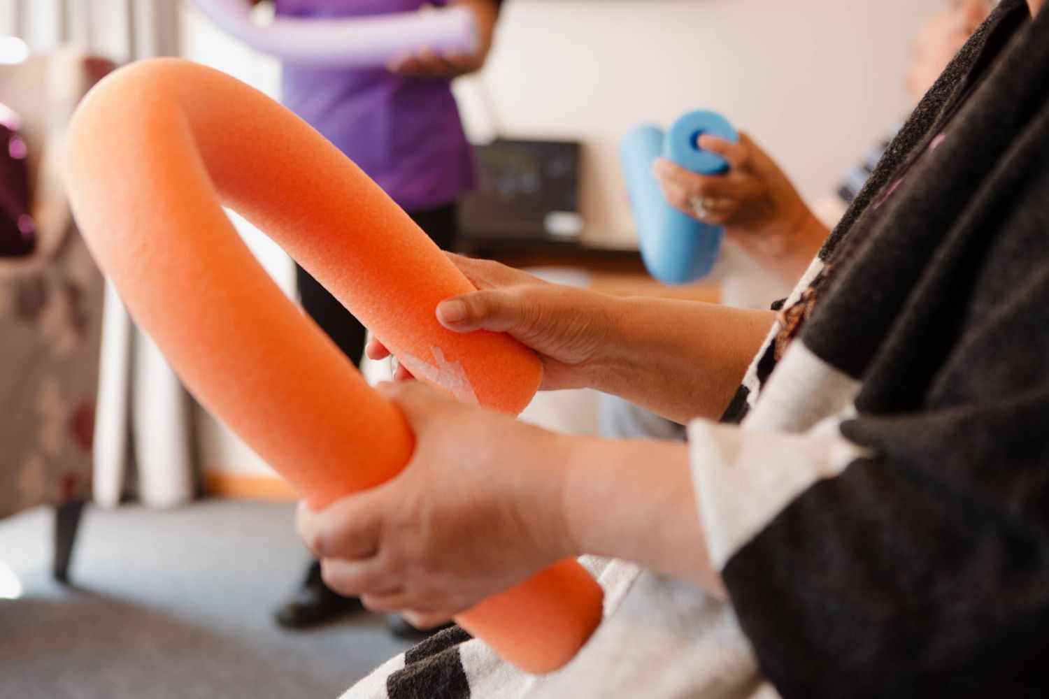 Close-up of hands holding orange pool noodles during an indoor activity session.
