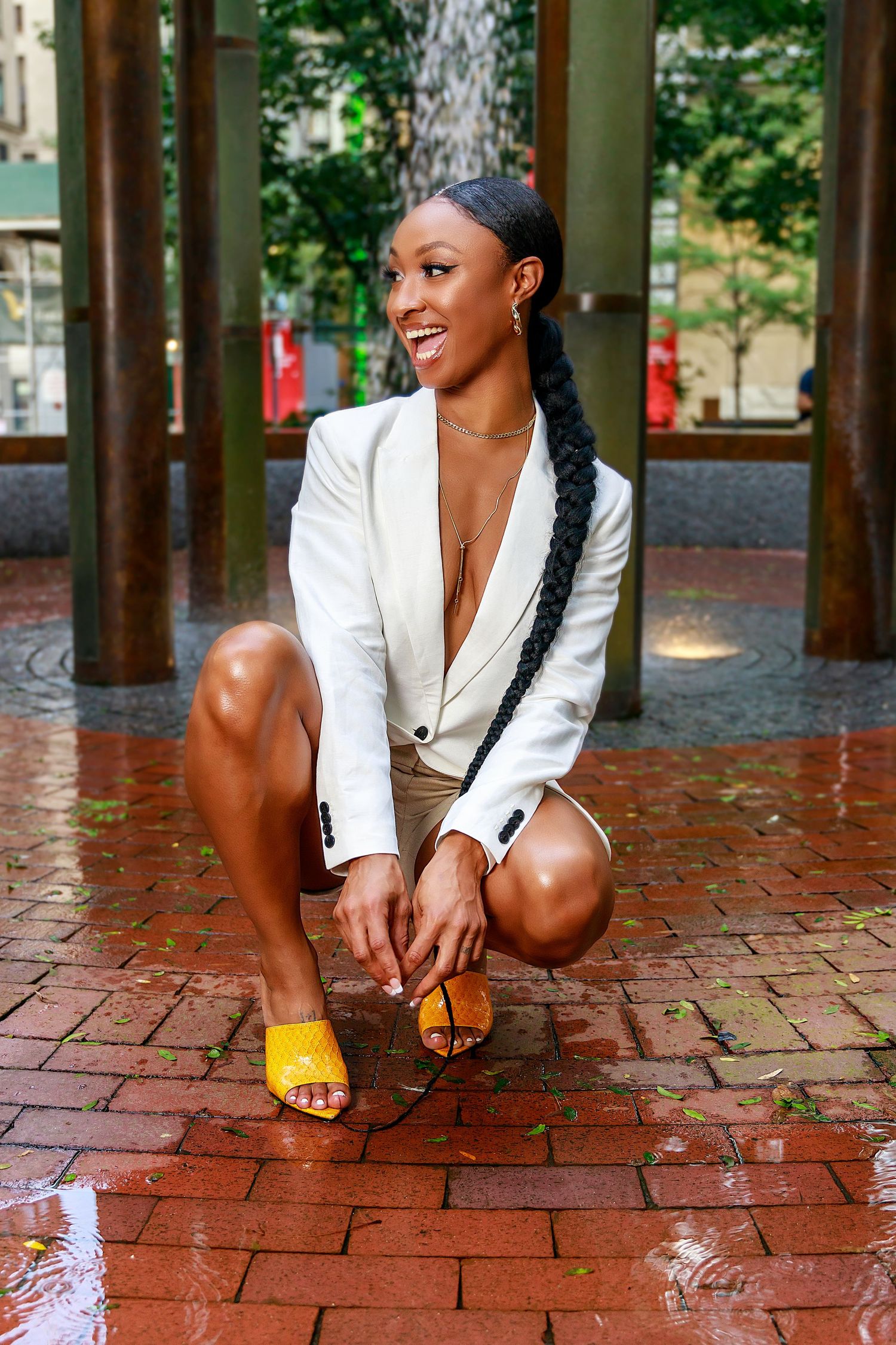 Professional fashion portrait in white blazer and casual wear on wet brick pavement.