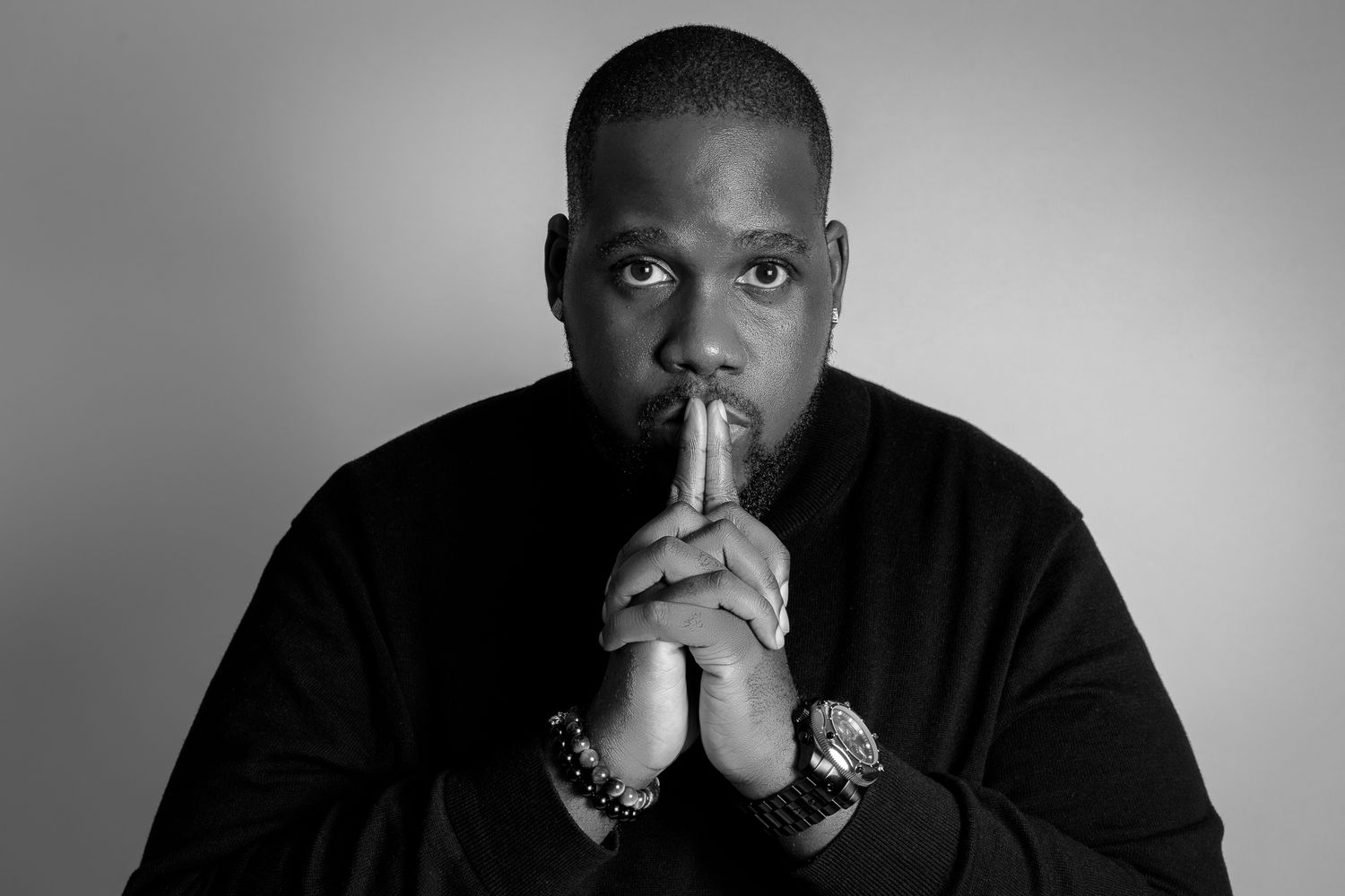 Dramatic black and white portrait of a person in contemplative pose wearing a black sweater.
