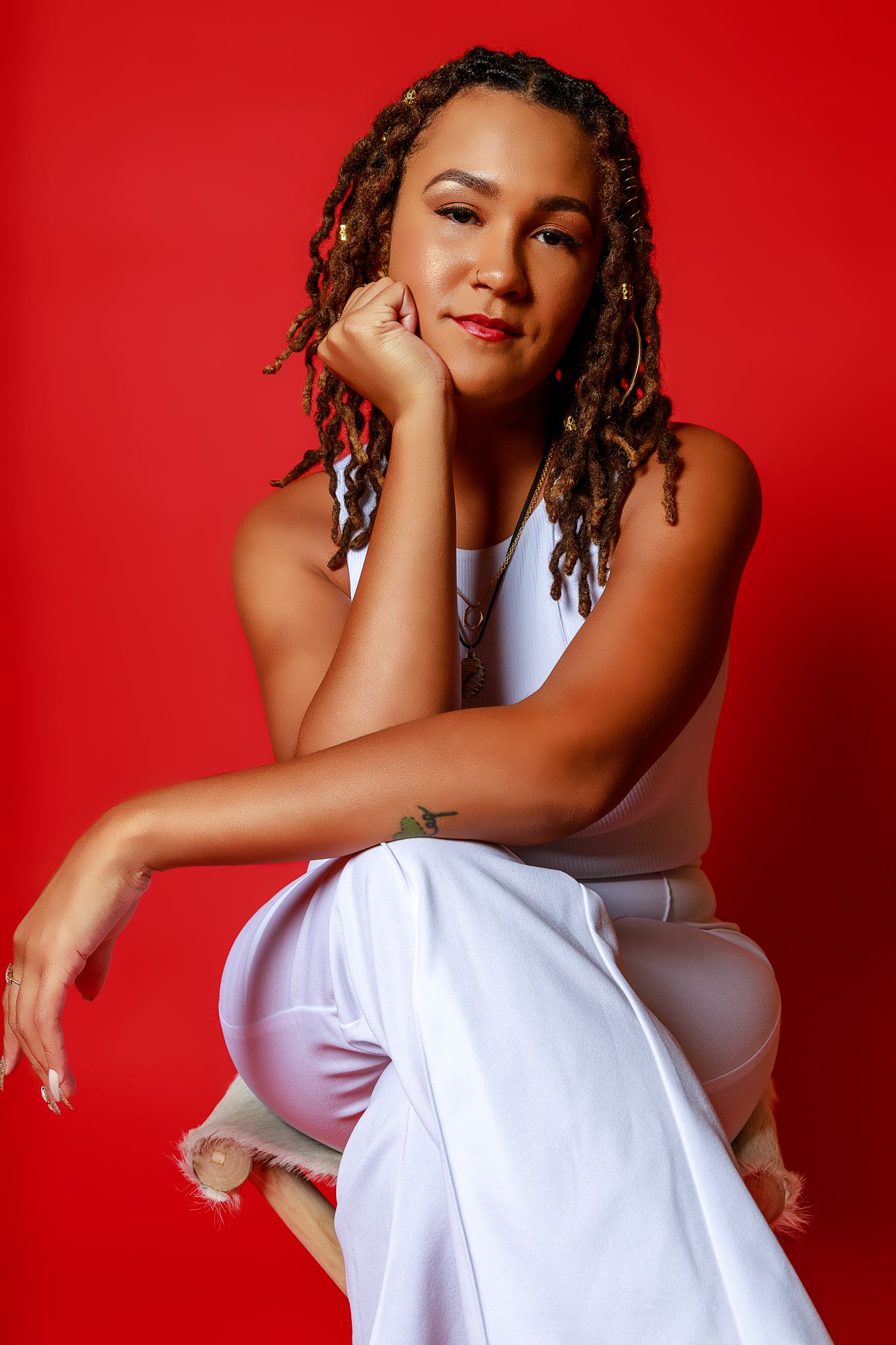 Portrait against vibrant red background featuring casual white outfit and natural hairstyle.