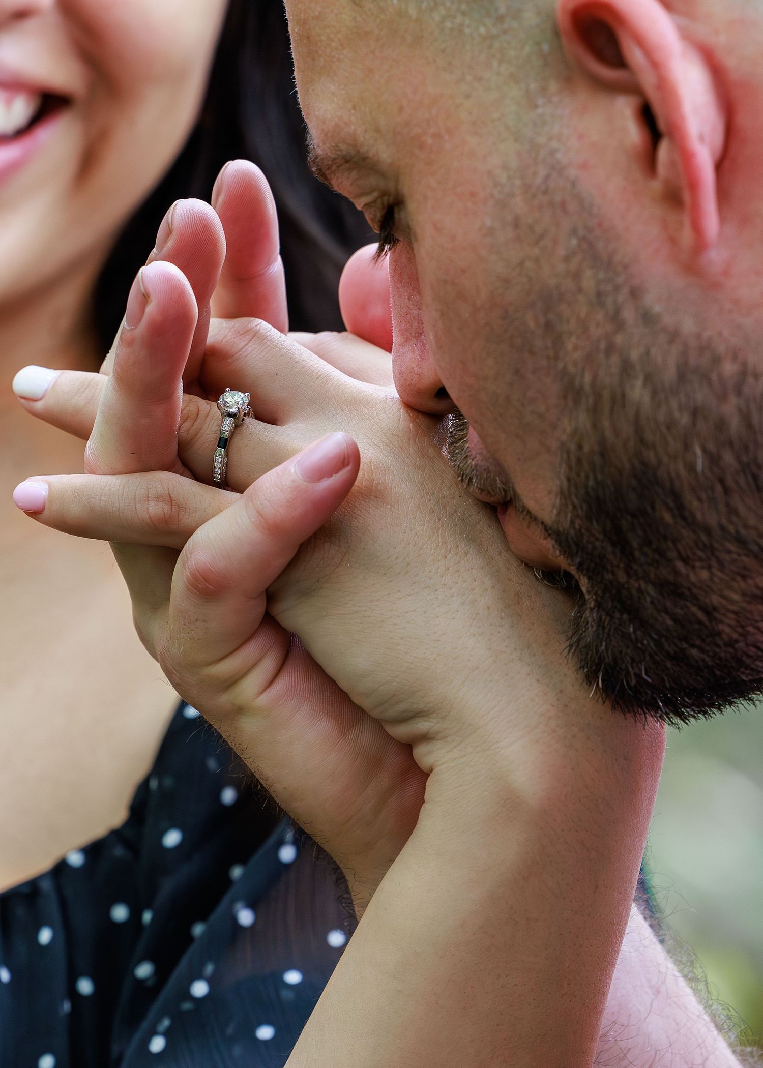 Close up of person with beard kissing someone's hand showing an engagement ring.