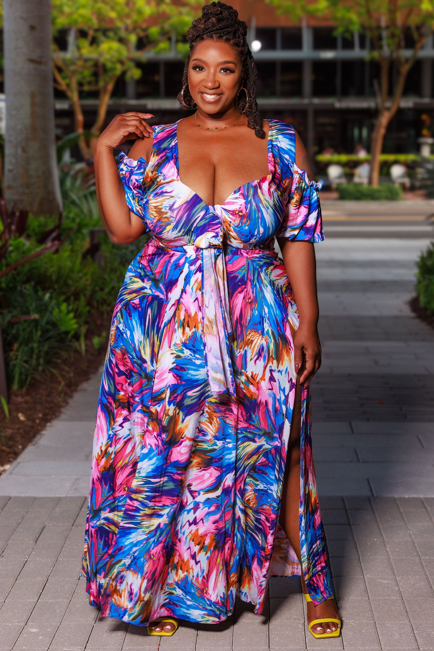 Curvy model in vibrant floral maxi dress with puff sleeves poses confidently on outdoor path.
