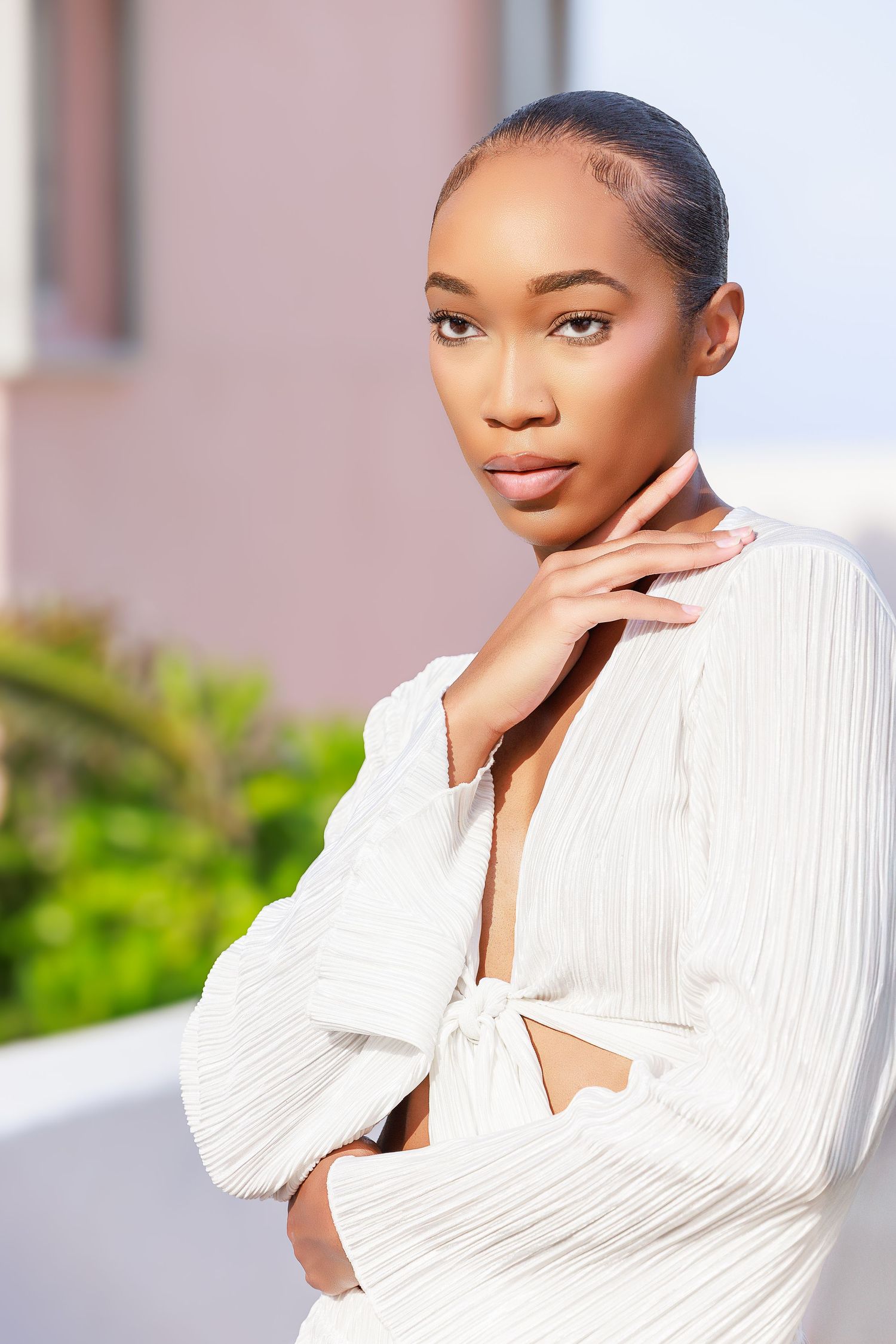 Elegant Black woman in white ribbed tie-front crop top posing outdoors with hand on chin, serene expression.