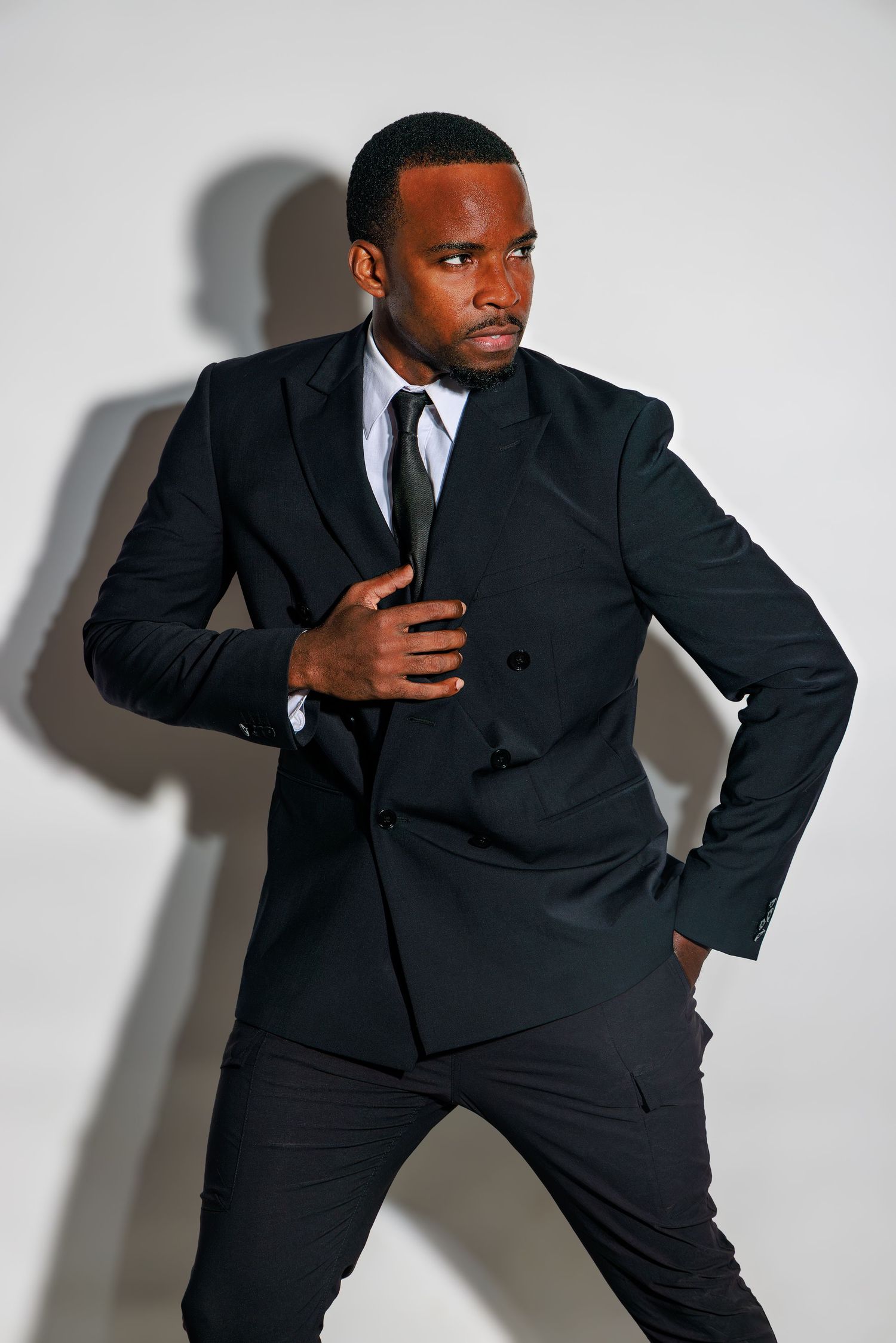 Professional model in black business suit striking dynamic pose against white studio background.