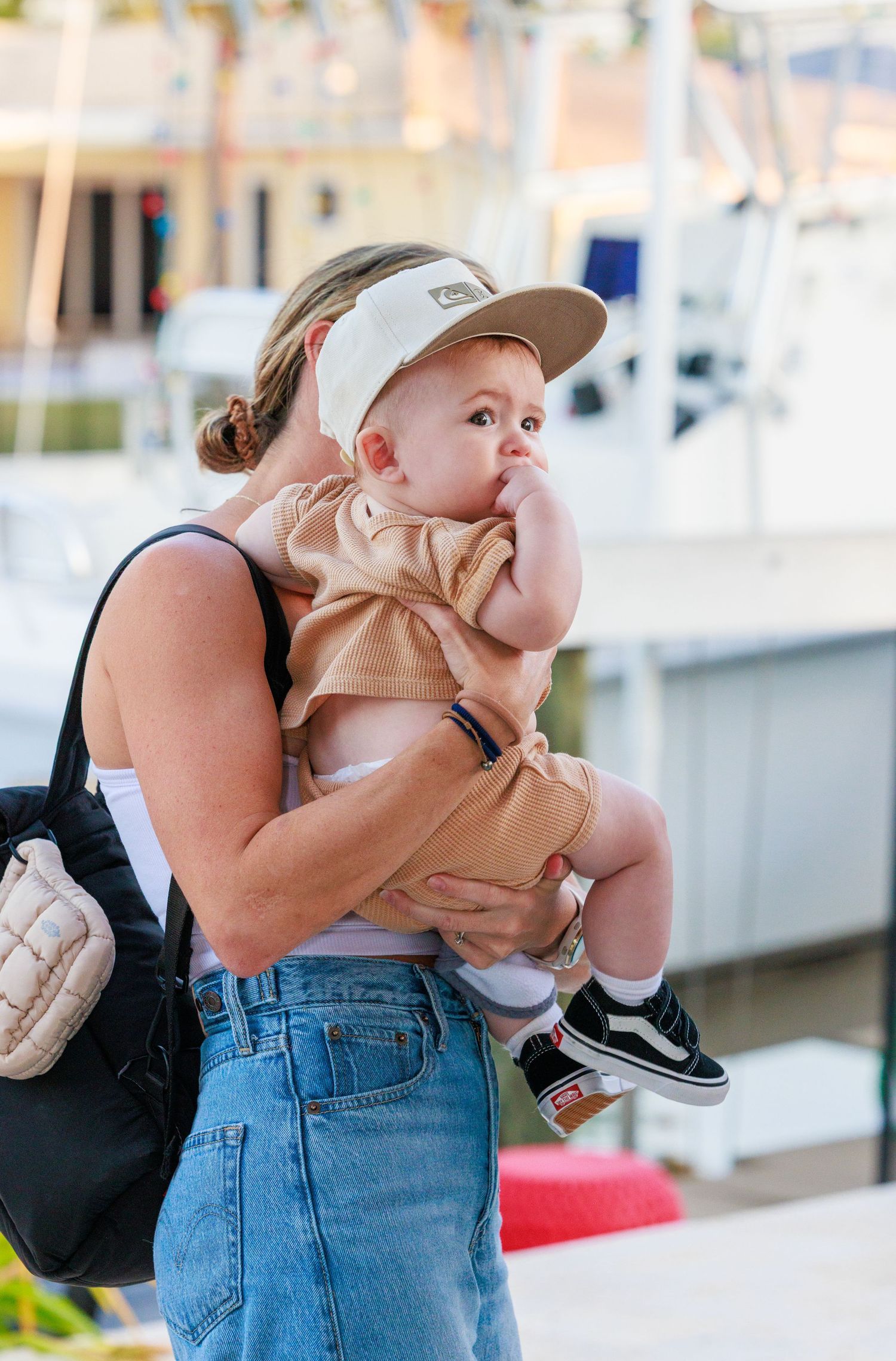A series of candid moments showing a person in denim overalls holding and feeding a baby outdoors near a marina.