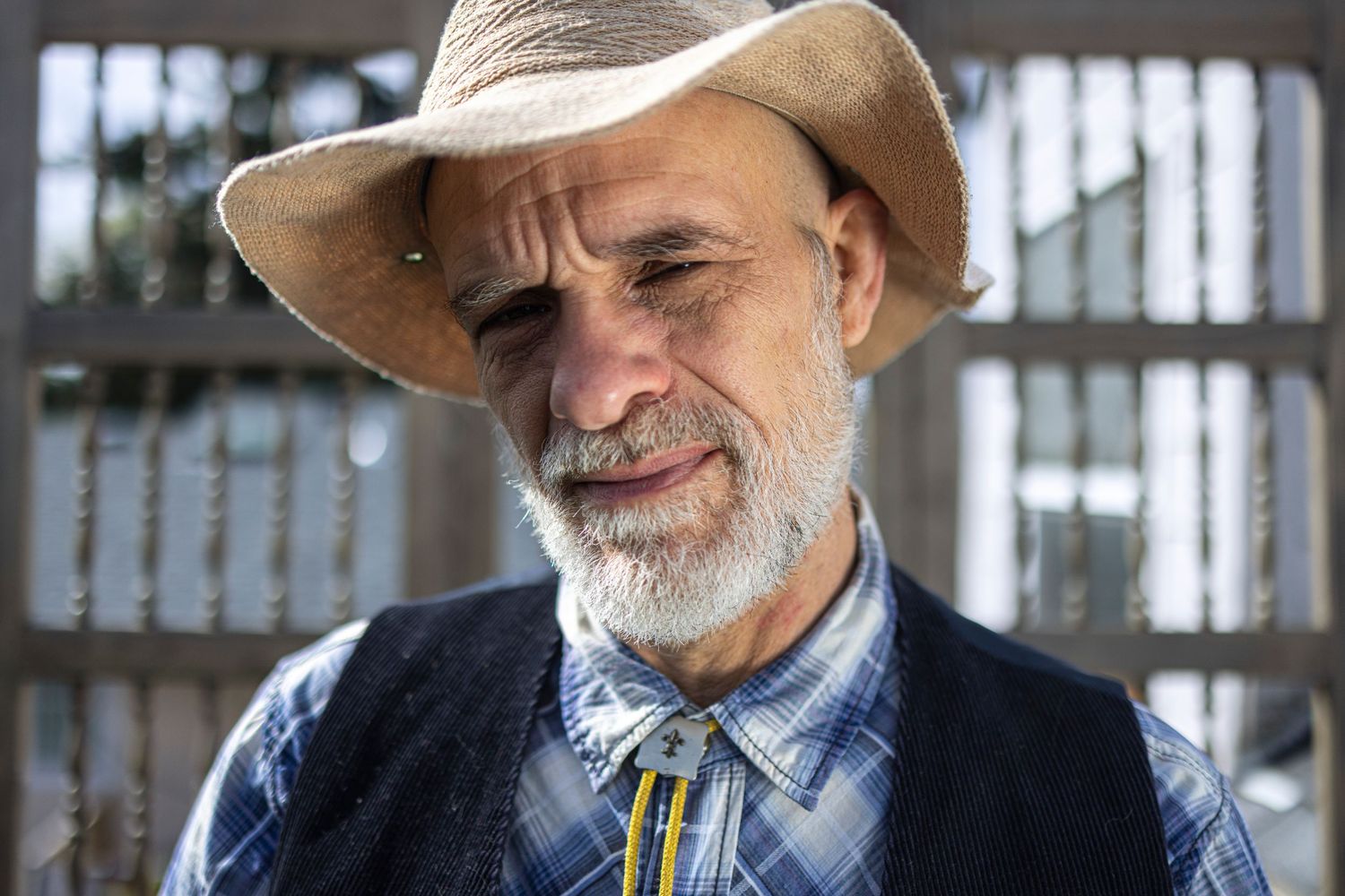 Closeup photo of a man with white beard, straw hat, and bolo tie outside on a sunny morning