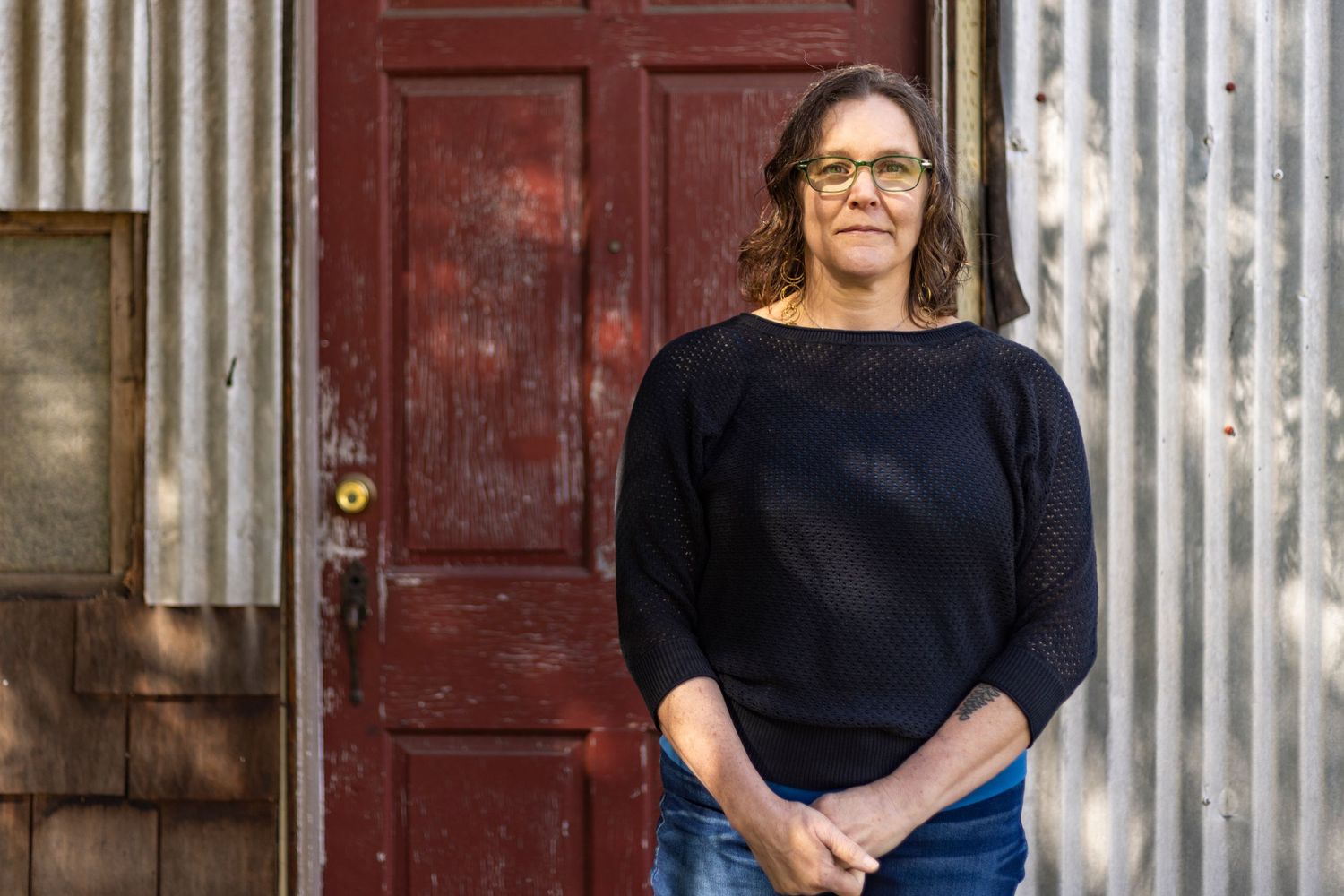 Photo of a woman wearing glasses in front of a barn door in dappled shade