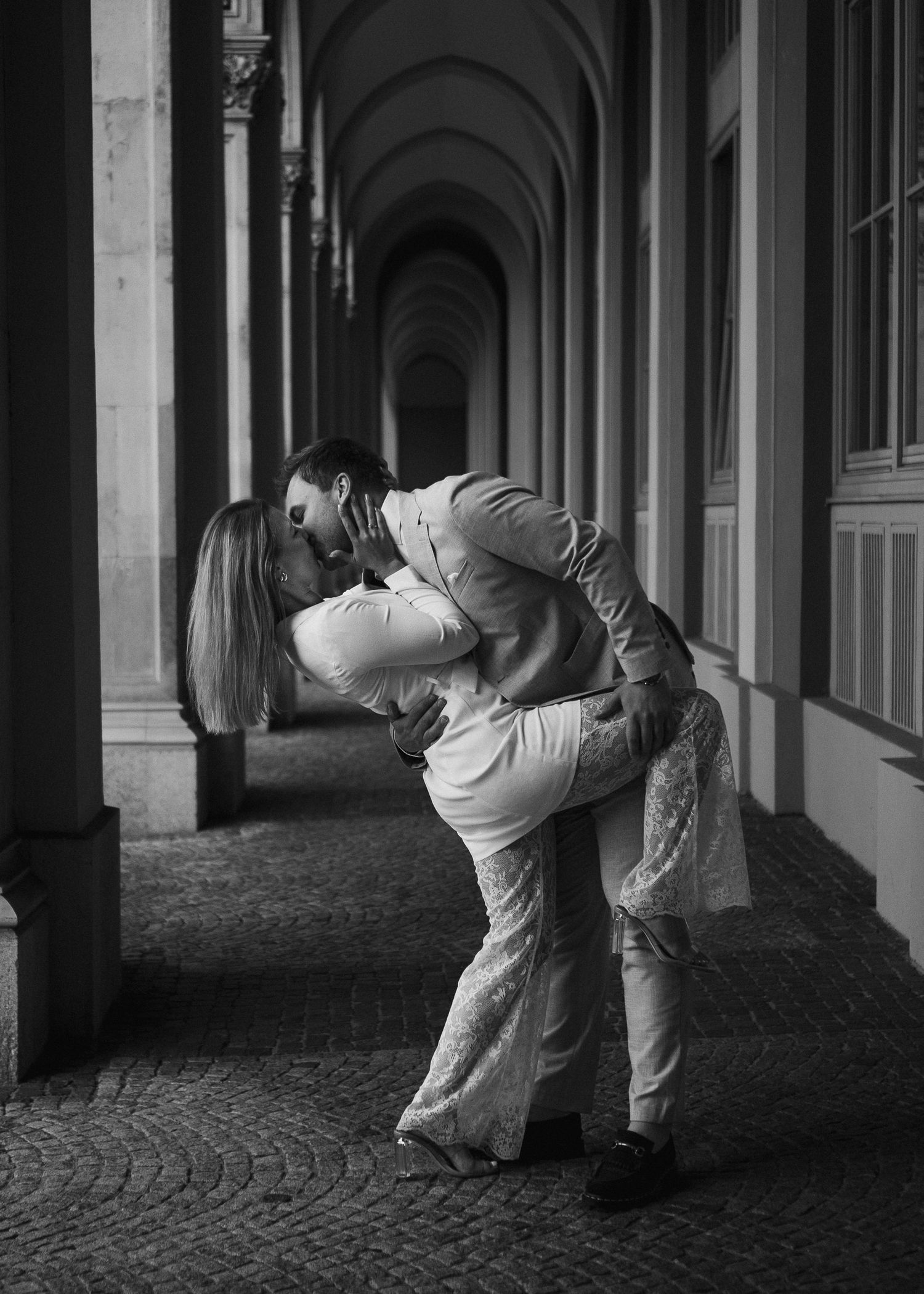 Filmreifer Hochzeitskuss: Der Bräutigam beugt die Braut in einer tiefen Umarmung in den historischen Arkaden von München zurück.