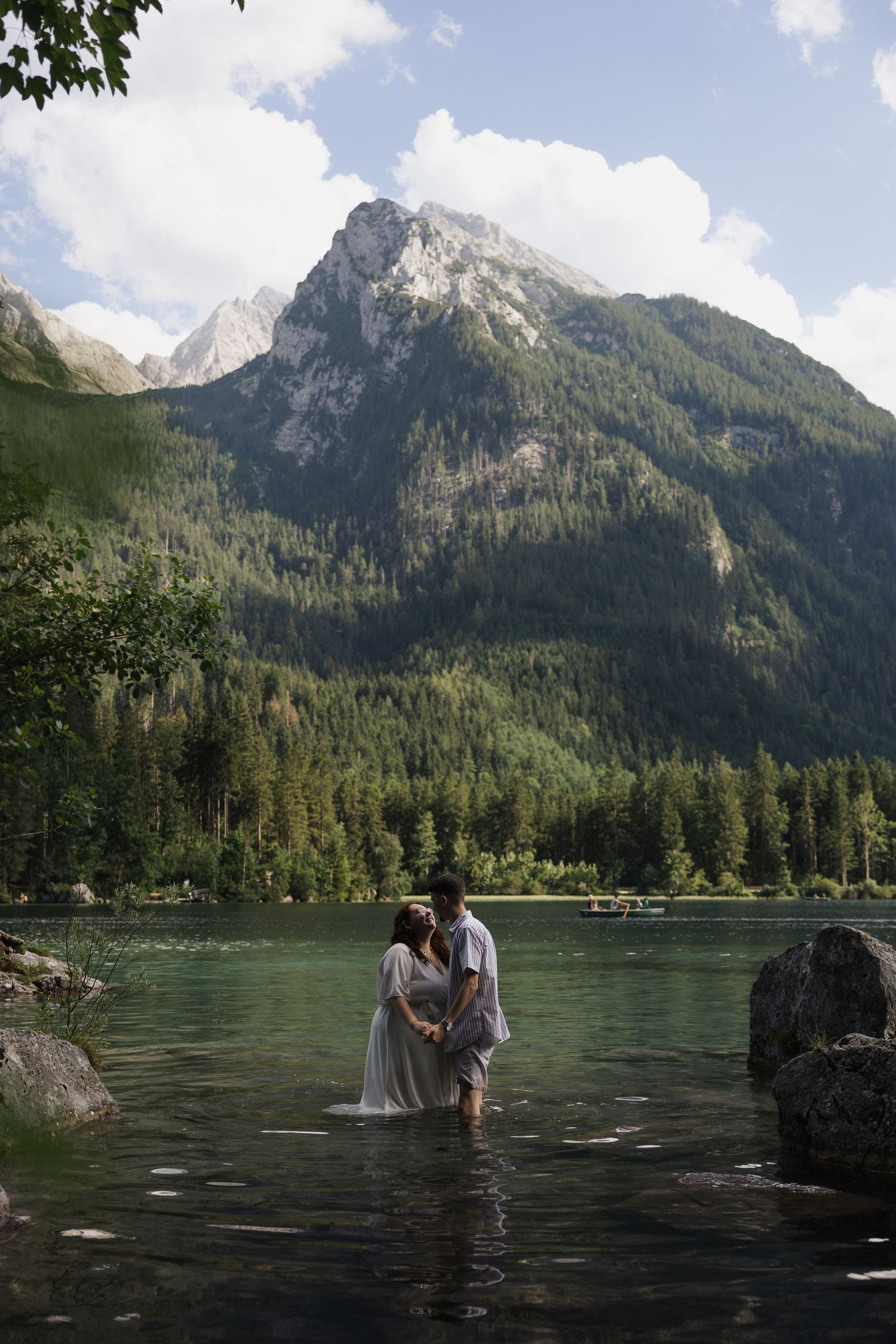 Ein Paar steht Hand in Hand im klaren Wasser des Hintersees vor einer monumentalen Bergkulisse, fotografiert von Ella Grinvalde Photography