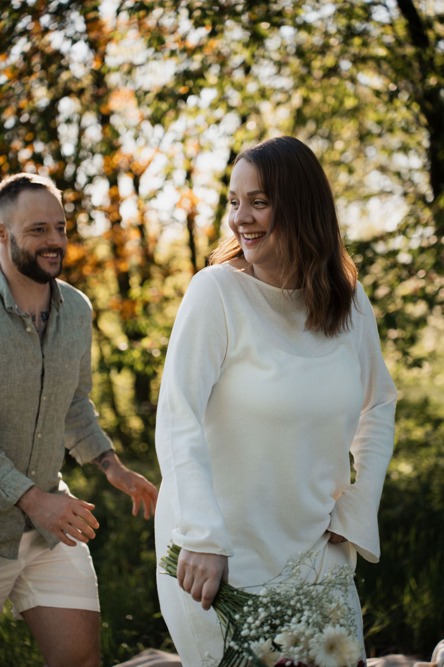 Glückliches Paar lacht während eines herbstlichen Outdoor-Shootings in Braunau, die Frau hält einen herbstlichen Blumenstrauß.