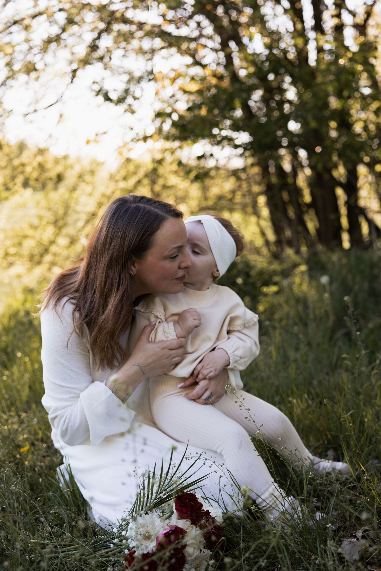 Herzliches Familienshooting in Braunau: Eine Mutter hält ihr kleines Kind liebevoll im Arm, während sie gemeinsam im hohen Gras einer sonnig