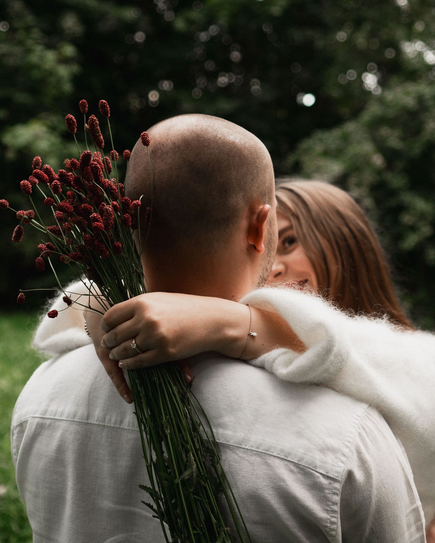 Romantisches Paar-Shooting in München: Braut blickt über die Schulter ihres Mannes, während sie einen herbstlichen Blumenstrauß hält.
