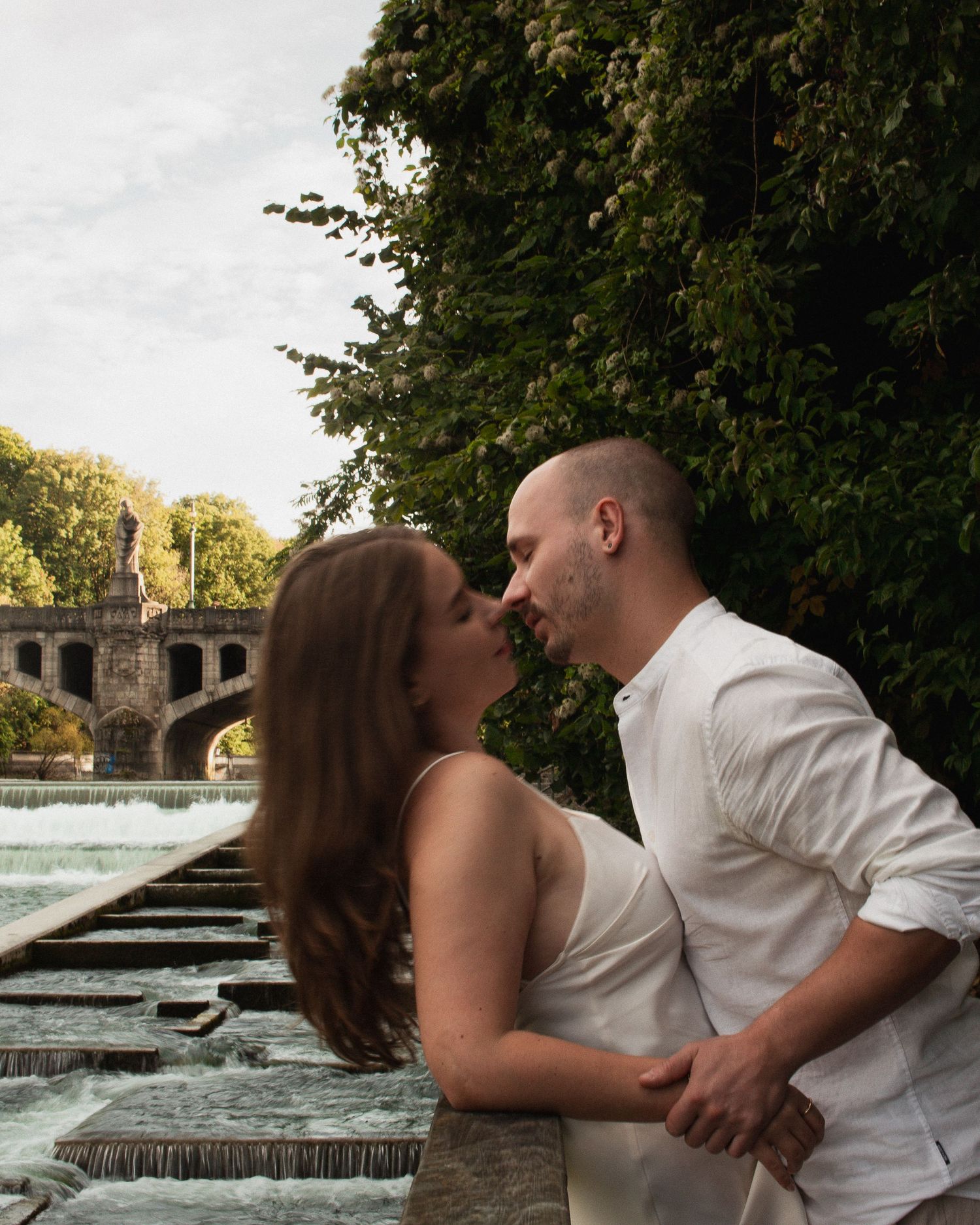 Hochzeitsfotografie an der Isar: Brautpaar küsst sich vor der Kulisse der Maximiliansbrücke und dem Isar-Wehr in München.