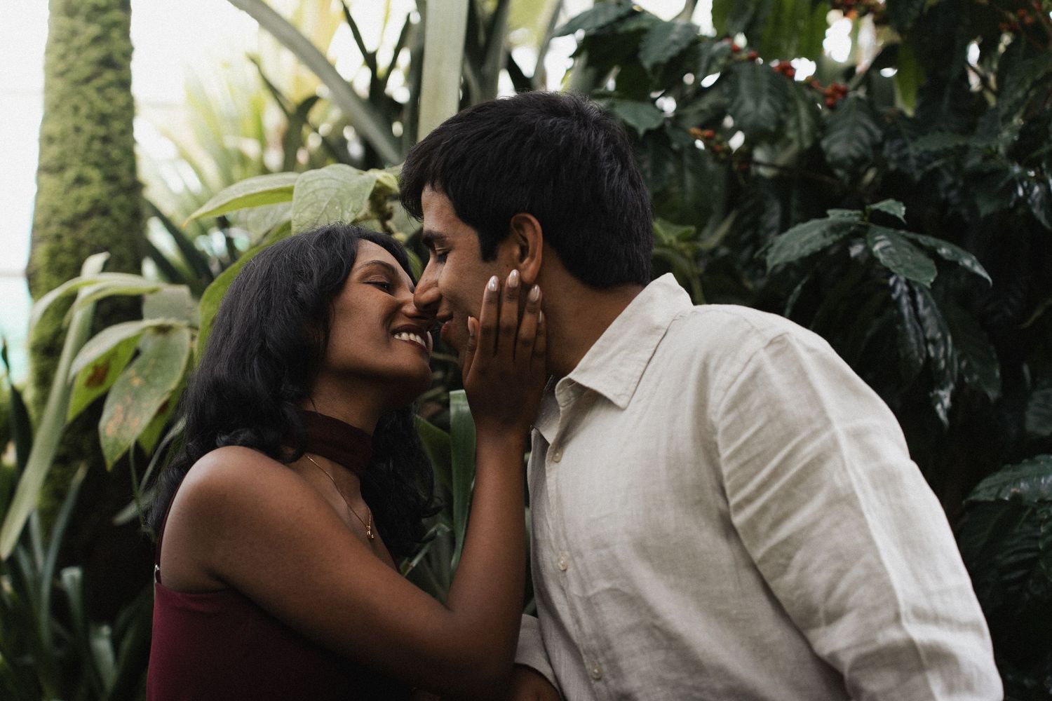 Engagement Shoot München: Lachendes Paar berührt sich zärtlich im Gewächshaus des Botanischen Gartens. Natürliche, romantische Paarfotos.