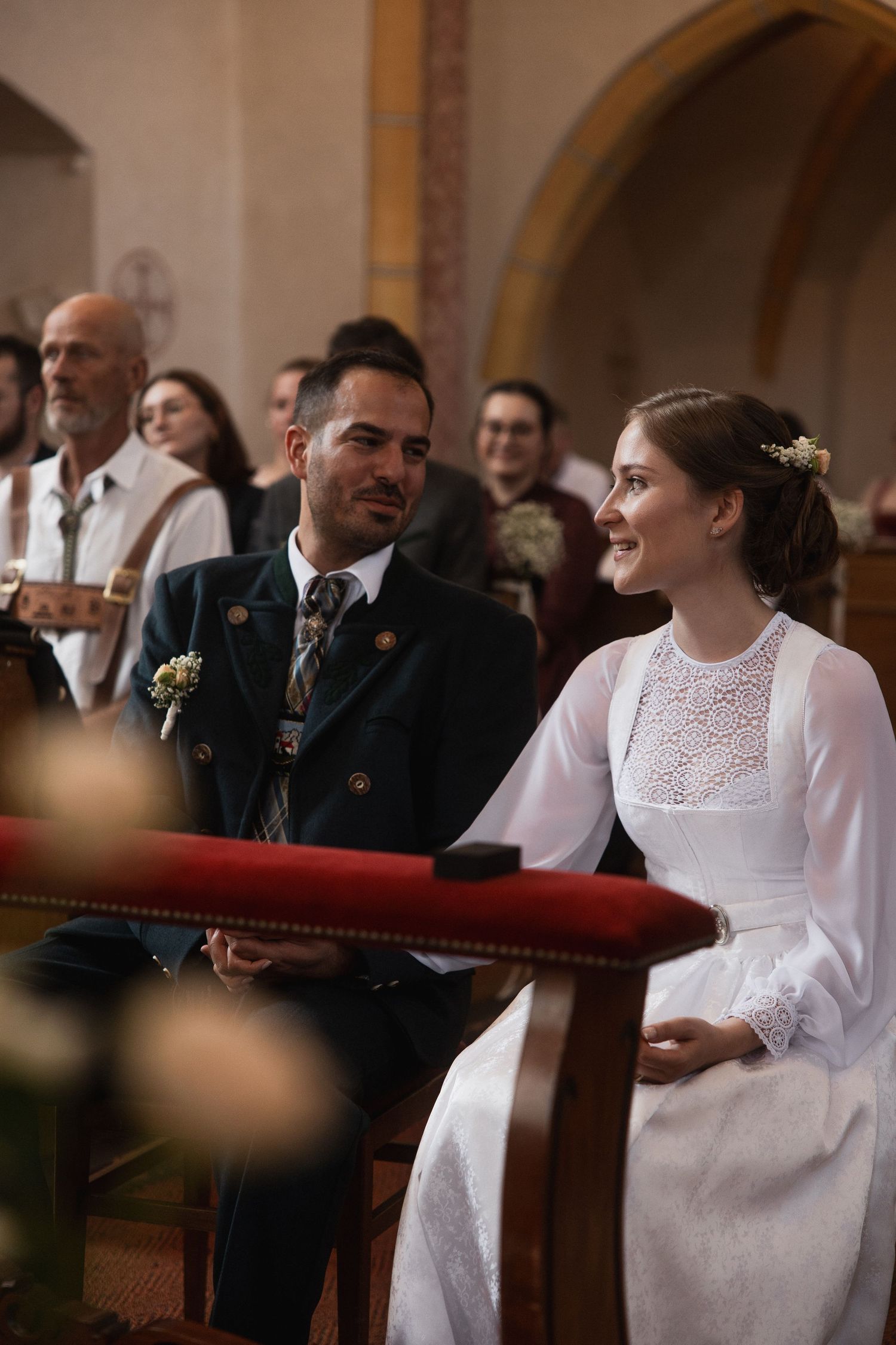 Trachten-Hochzeit in Bad Griesbach: Brautpaar blickt sich während der kirchlichen Trauung glücklich und verliebt an.