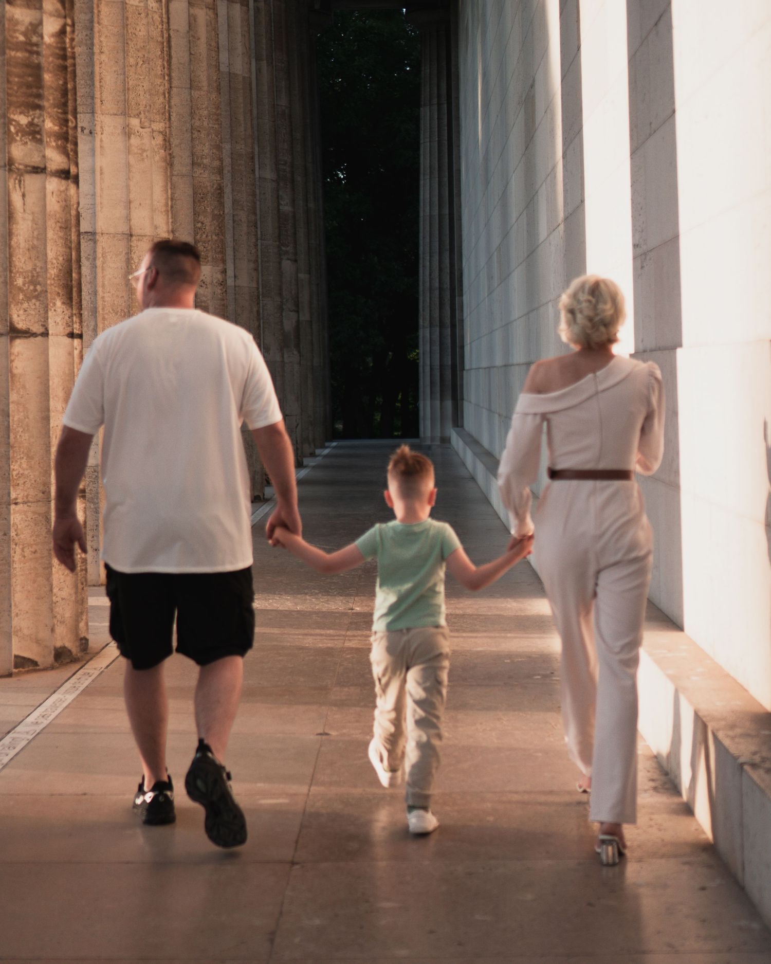 Familienfotografie an der Walhalla Regensburg: Ein Paar geht Hand in Hand mit seinem kleinen Sohn durch die monumentalen Säulengänge des Den