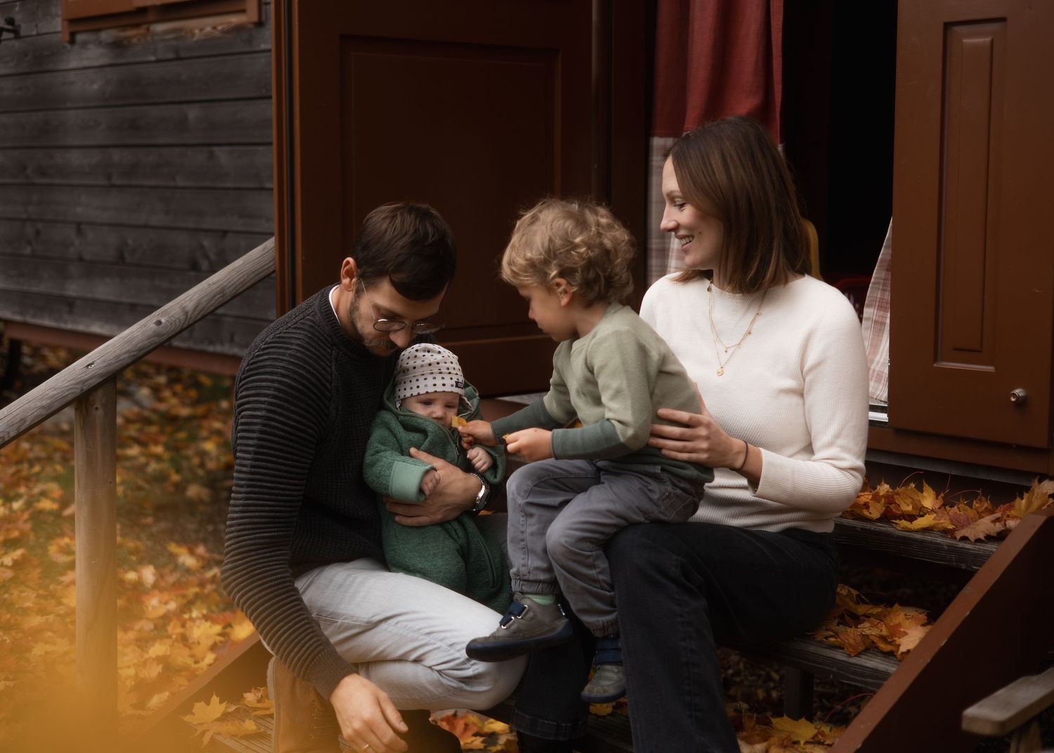 Authentische Familienmomente im Herbst: Eltern sitzen mit ihren zwei Kindern auf den Stufen eines Holzwagens am Arterhof.