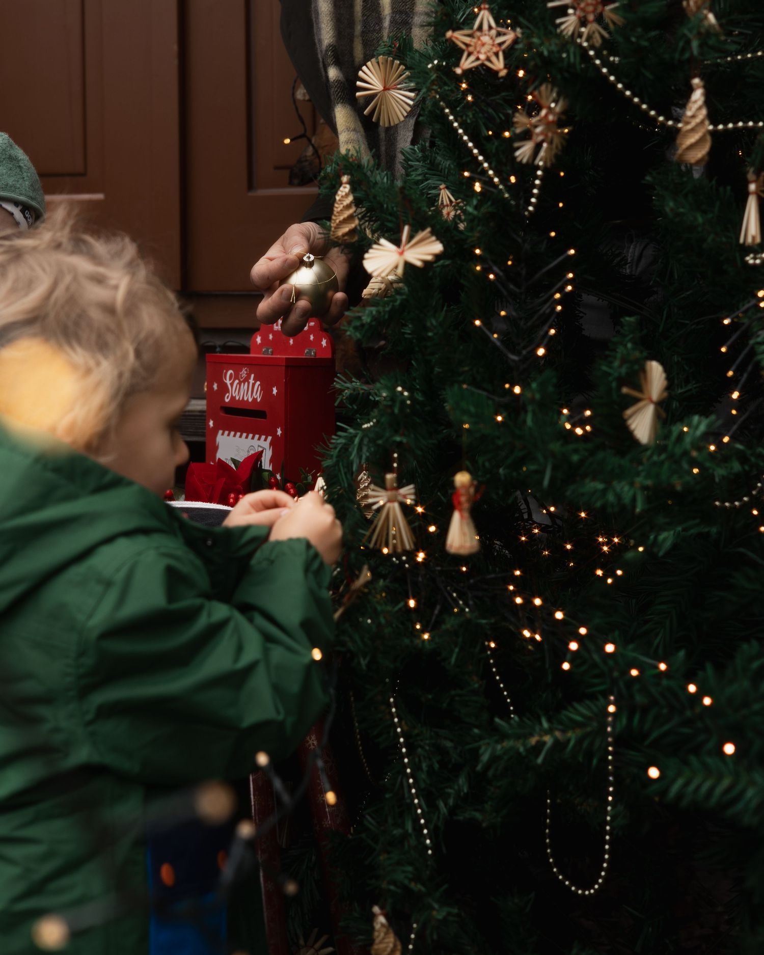 Weihnachtliche Familienfotografie in Bad Birnbach: Ein kleiner Junge dekoriert konzentriert einen Tannenbaum vor einer rustikalen Kulisse.