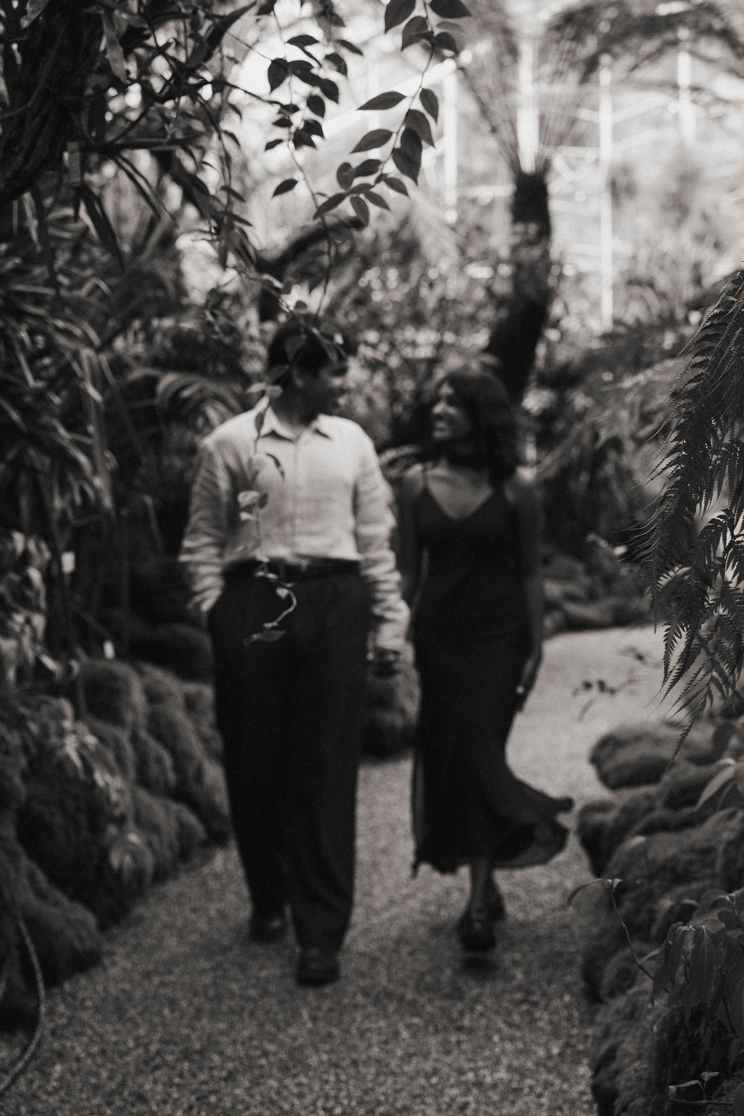 Schwarz-Weiß-Paarshooting: Paar läuft unscharf im Hintergrund durch das Gewächshaus im Botanischen Garten München. Cinematic Kunstfoto.