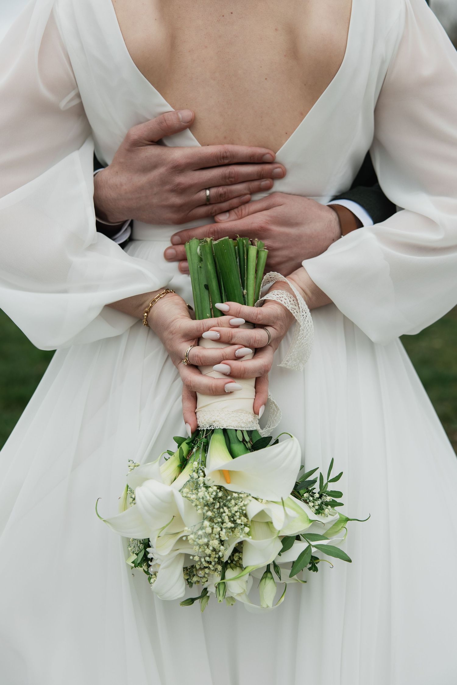Fine Art Hochzeitsfotografie: Der Bräutigam hält die Braut von hinten umschlungen, während sie ihren Calla-Strauß hält.
