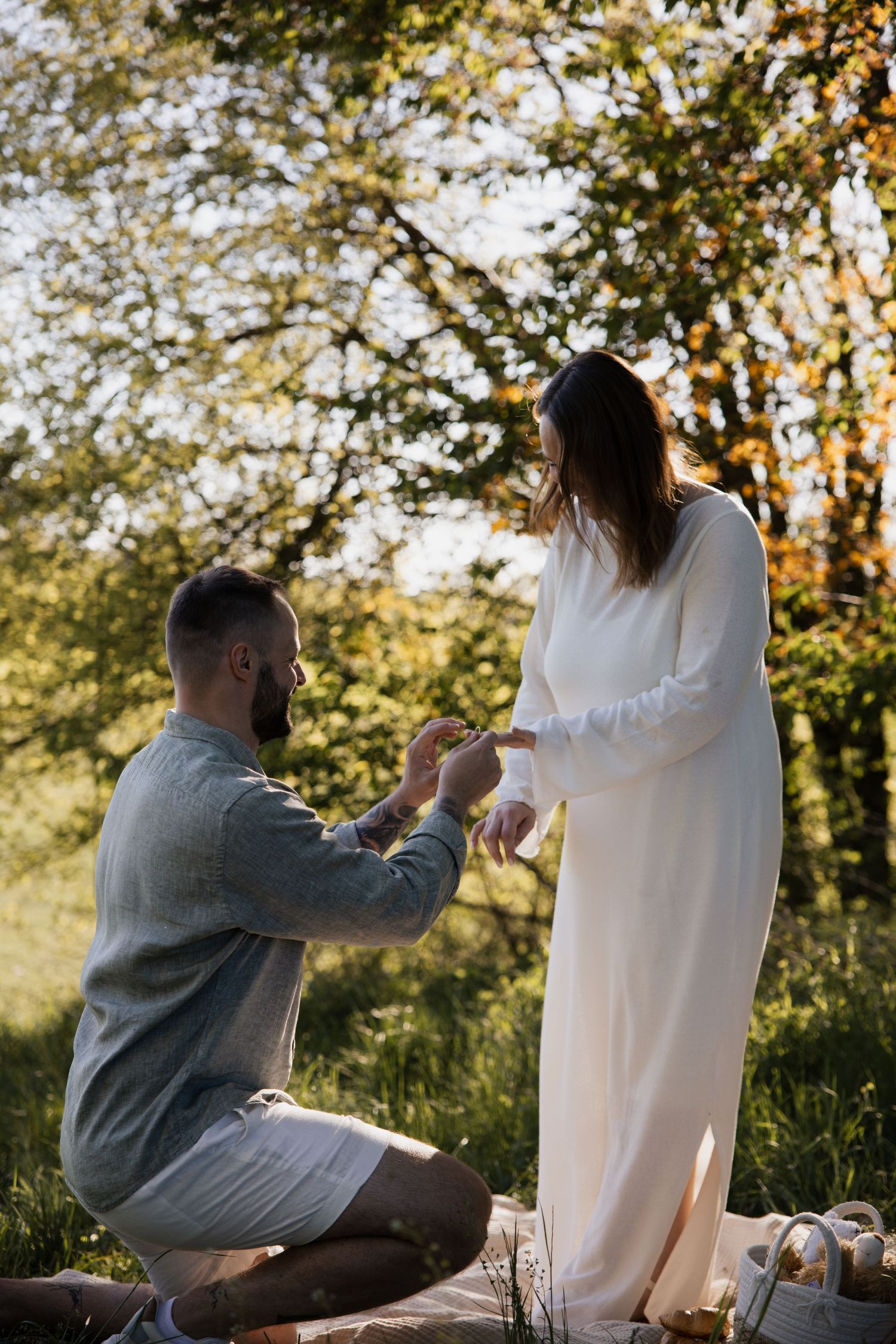 Der Moment des Heiratsantrags: Ein Mann kniet vor seiner Partnerin im Wald während eines Überraschungsantrags beim Fotoshooting.