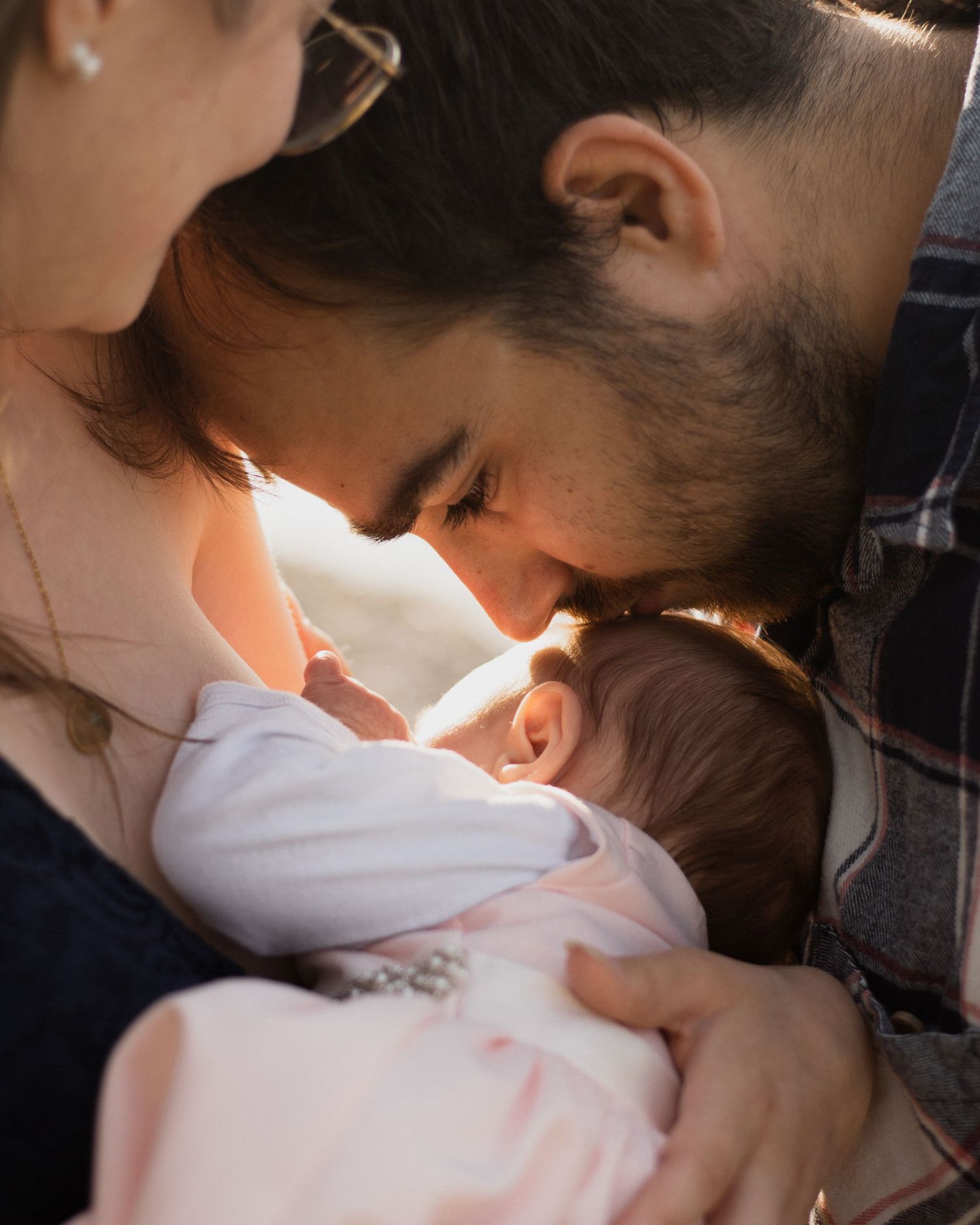 Emotionale Familienmomente: Vater gibt seinem neugeborenen Baby einen sanften Kuss auf die Stirn, eingefangen im warmen Gegenlicht.