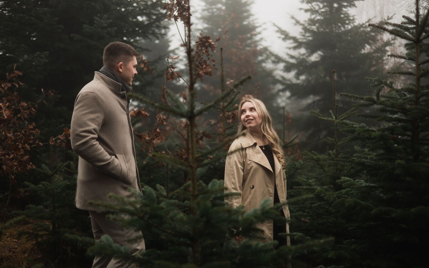Stimmungsvolles Winter-Shooting: Ein Paar spaziert zwischen Tannenbäumen auf einer Weihnachtsbaumfarm in Bad Birnbach bei nebligem Wetter.