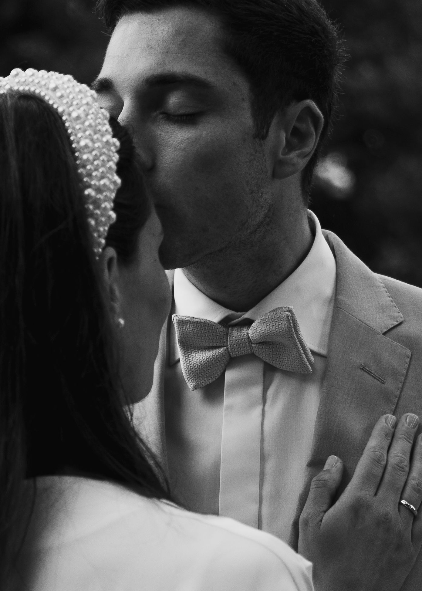 Intime Hochzeitsmomente: Der Bräutigam gibt der Braut einen sanften Kuss auf die Stirn; Fokus auf dem eleganten Perlen-Haarreif.