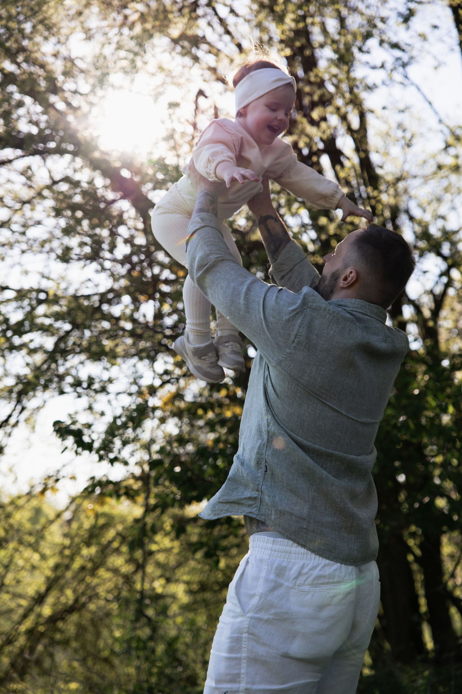 Fröhliche Familienfotografie in Braunau: Ein Vater hebt sein lachendes Kind im Gegenlicht der Abendsonne spielerisch in die Luft.