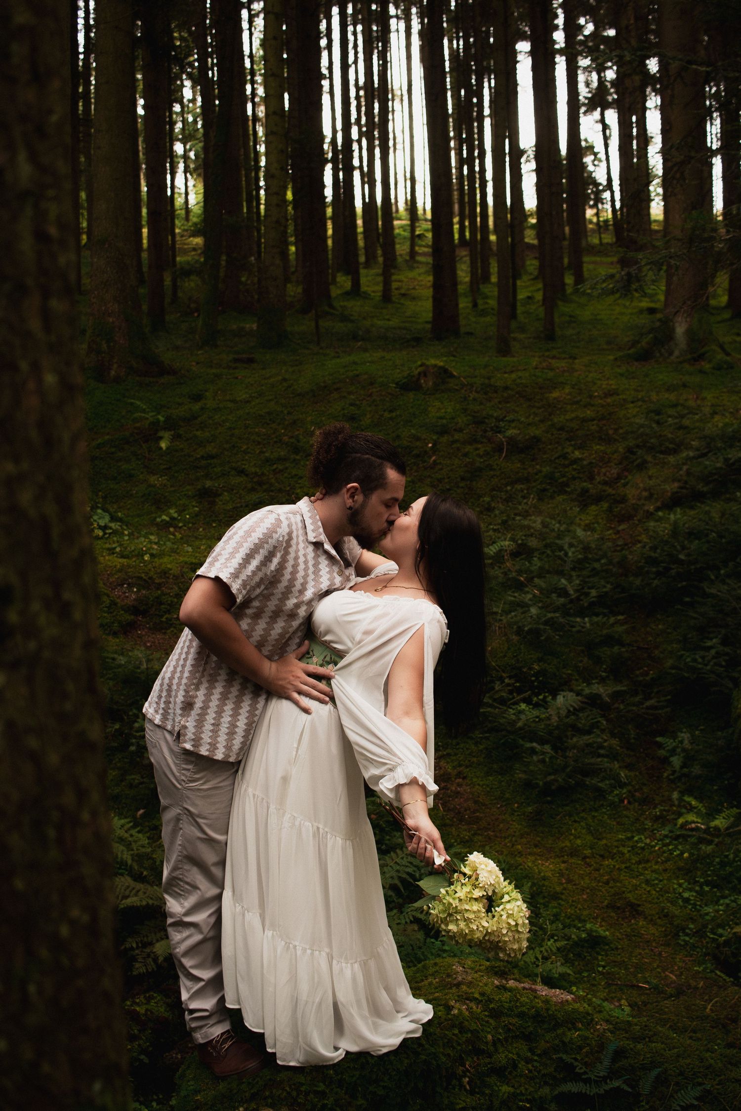 Inniger Kuss eines Paares in einem dichten Wald bei Bad Birnbach; Braut im weißen Kleid mit Blumenstrauß.