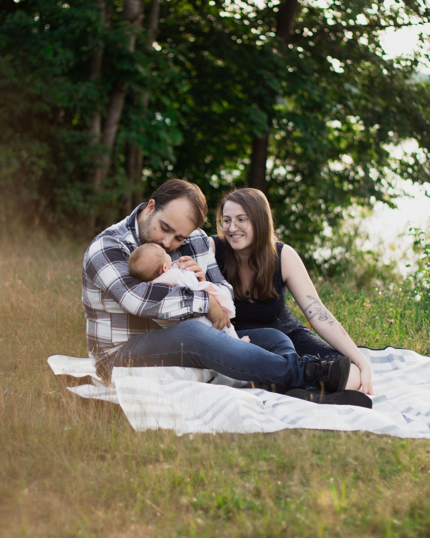 Entspanntes Familienshooting am See bei Pfarrkirchen: Eltern sitzen mit ihrem Baby auf einer Picknickdecke im Grünen.