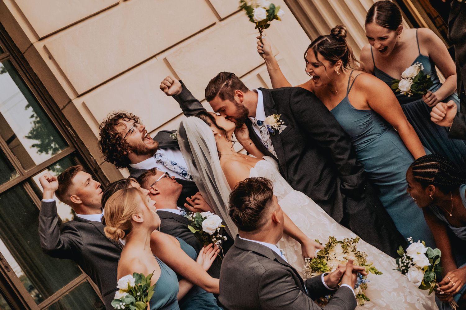 Wedding party laughs together while holding bouquets and posing for candid photos during celebration.