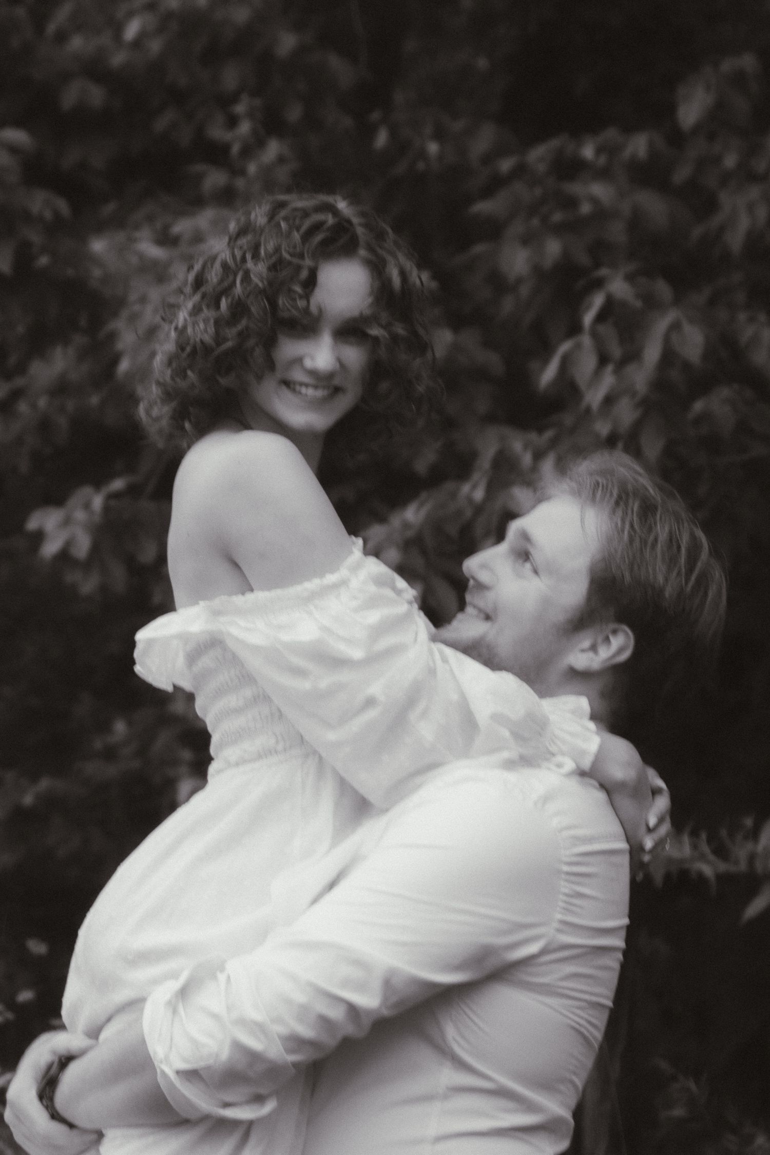 A series of black and white photos showing a couple embracing and sharing joyful moments outdoors.