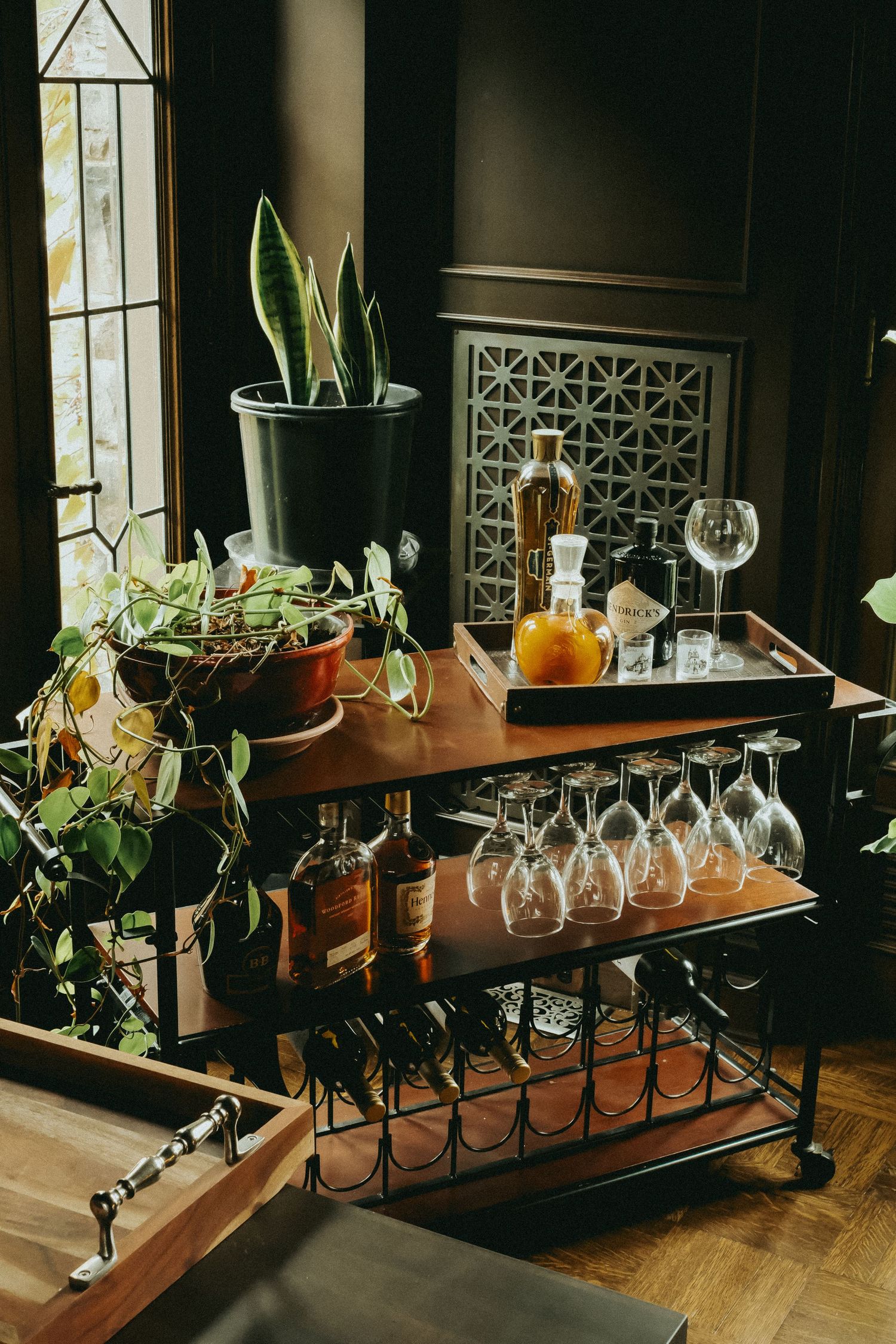 Empty wine glasses lined up on wooden shelves with green plants in a dimly lit restaurant interior.