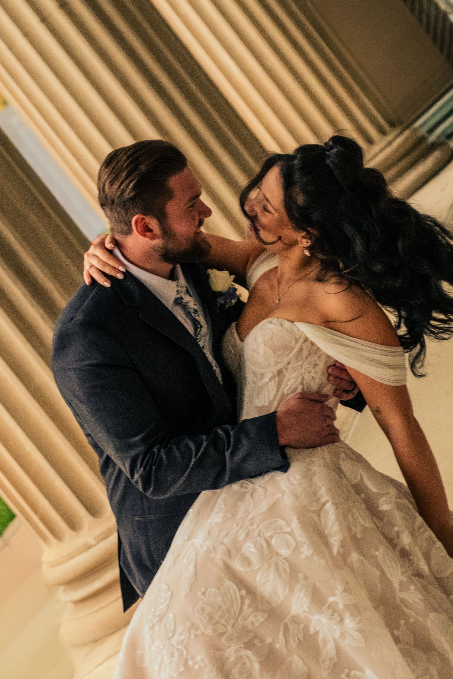 A romantic moment between newlyweds dancing at their wedding reception, with the bride in an off-shoulder white gown.