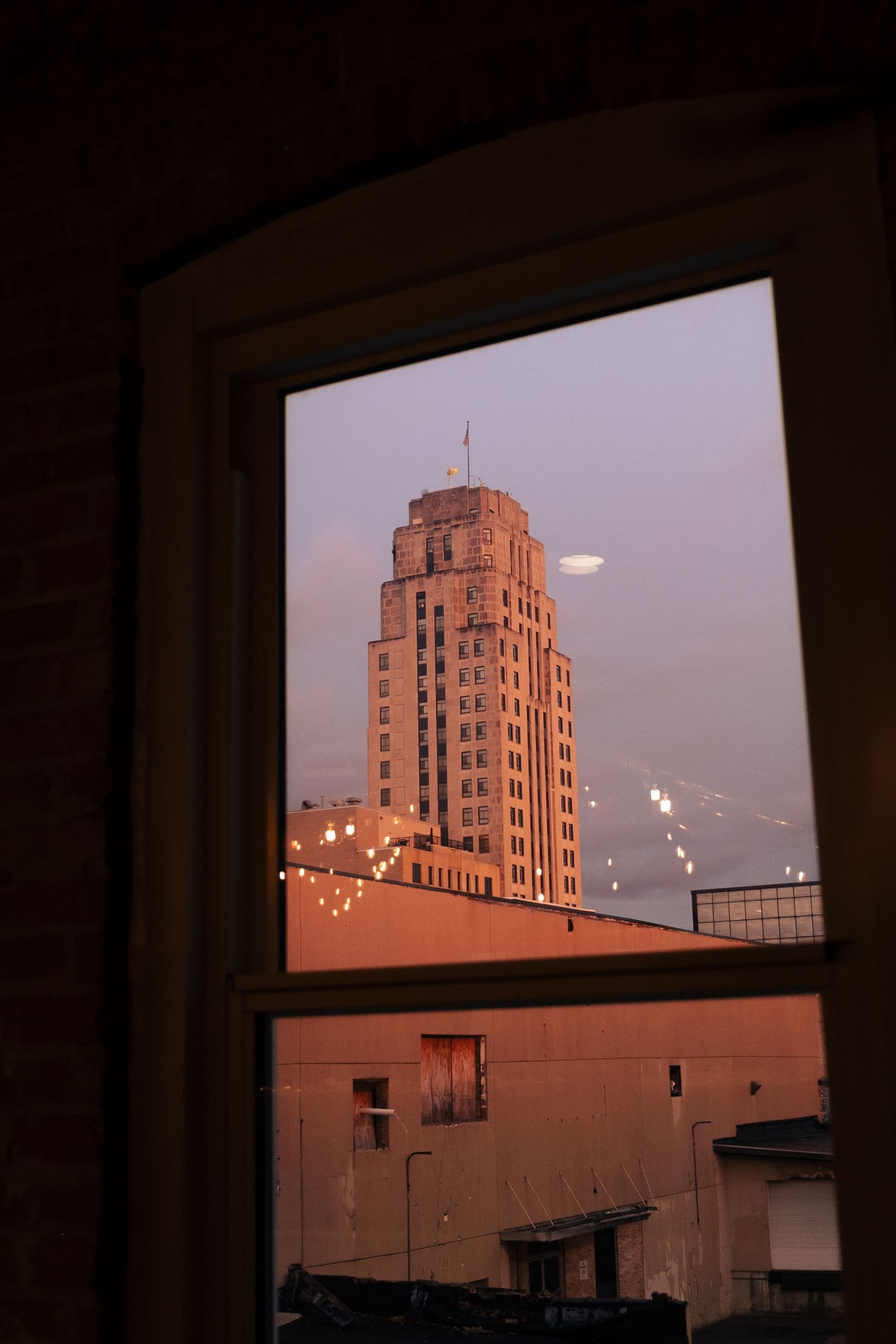 Art deco skyscraper photographed through window frames at sunset with warm orange lighting in urban setting.