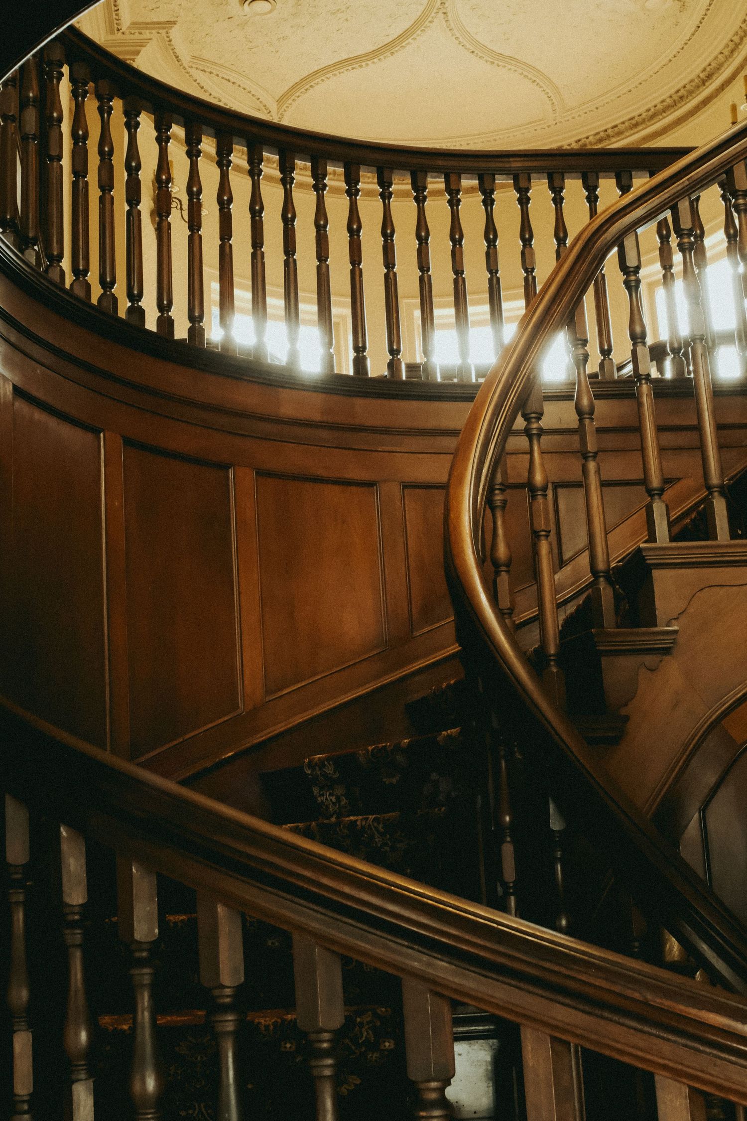 Elegant curved wooden staircase with ornate balusters and rich mahogany paneling in a grand historic interior.