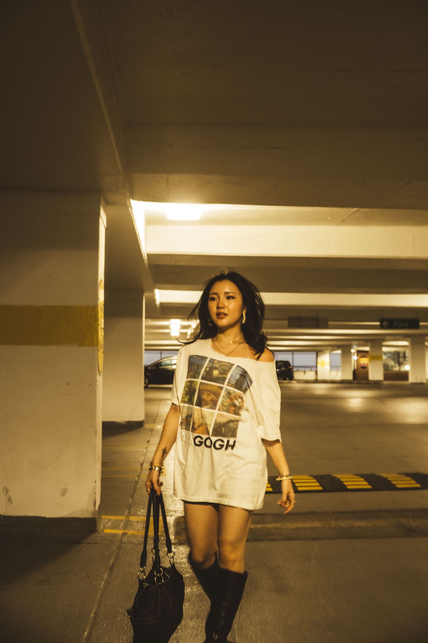 A person in casual attire poses expressively in a dimly lit parking garage with artistic lighting effects.