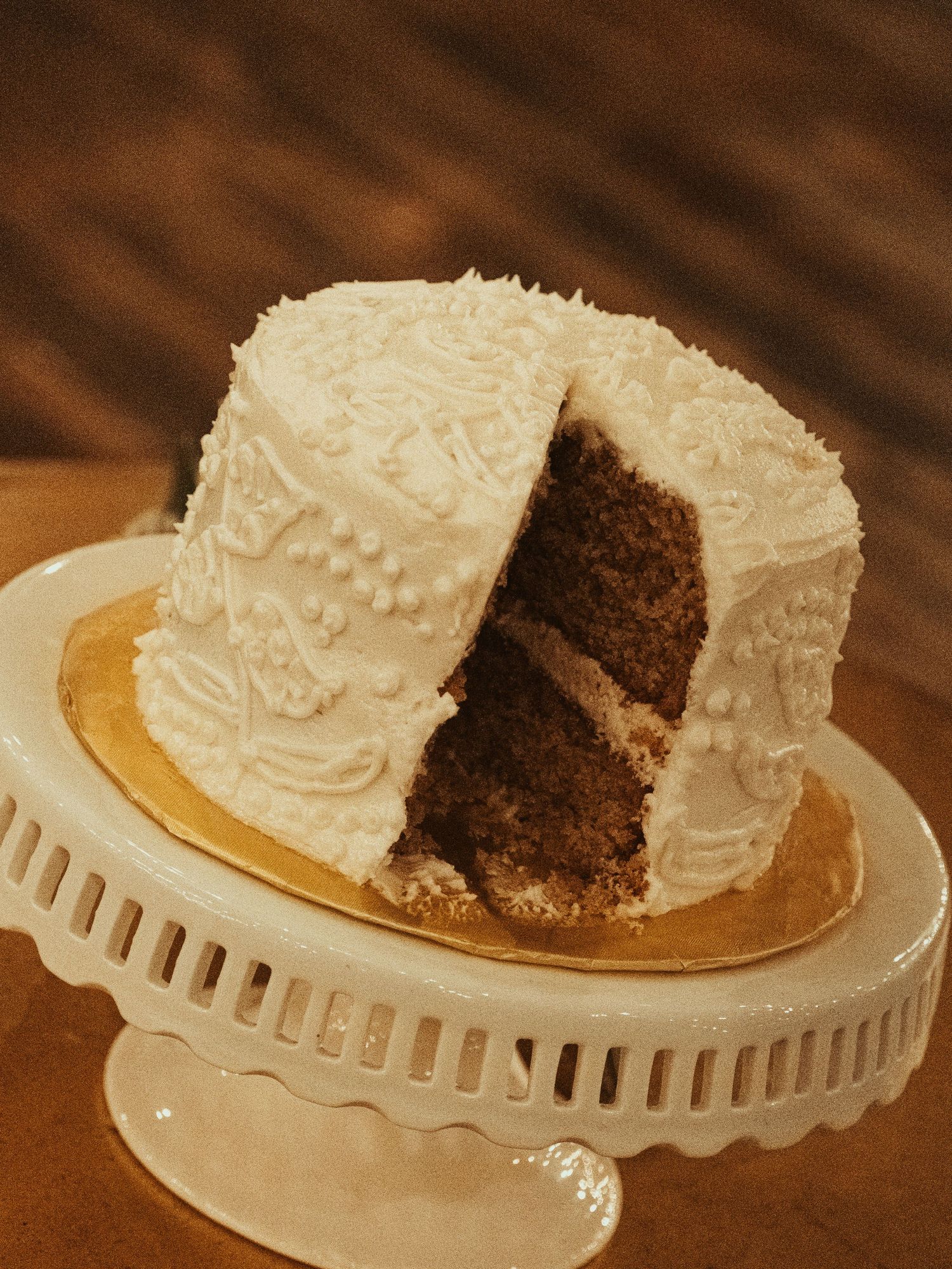 A chocolate cake with white frosting is displayed on a decorative white cake stand from multiple angles.