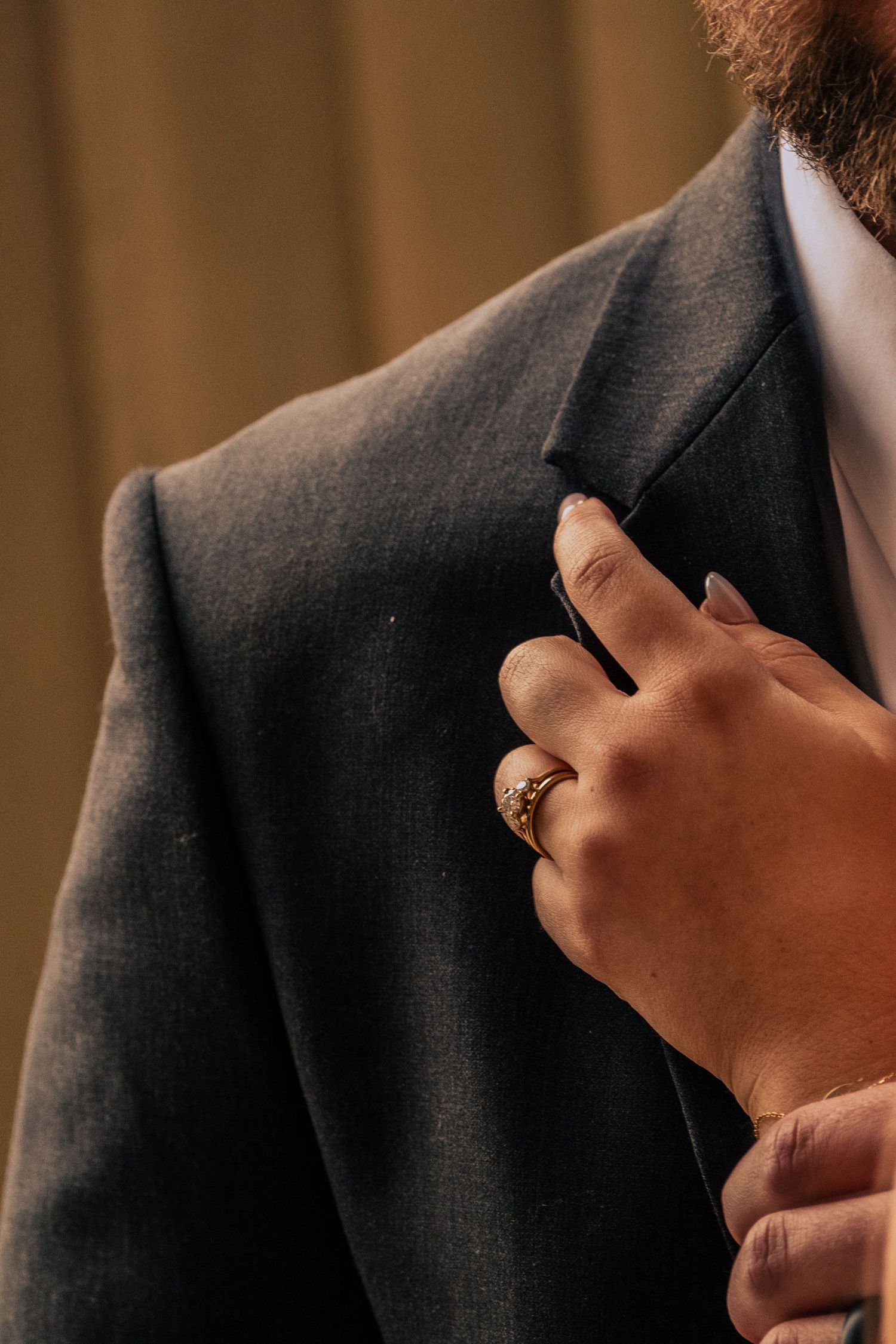 Close-up shot of hands adjusting a black suit jacket sleeve in warm lighting.